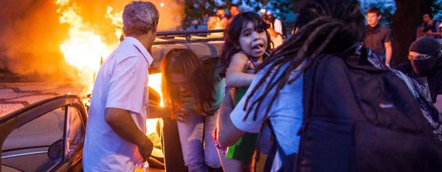 People help a family out of a burning car after it drove over a barricade of fire started by protesters, during demonstrations against the staging of the upcoming 2014 World Cup