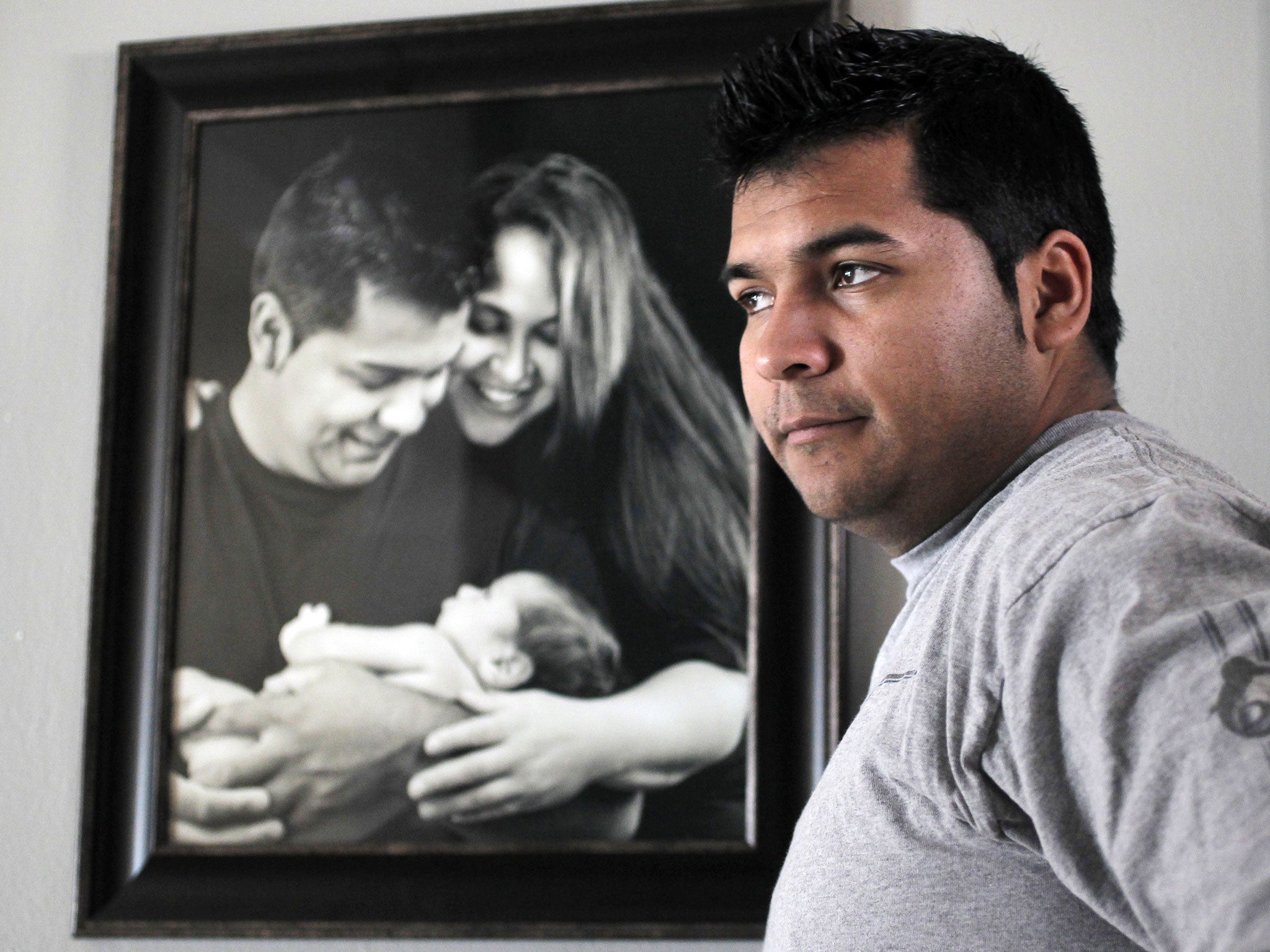 Erick Munoz stands with a photograph of himself, left, with wife Marlise and their son Mateo (AP)