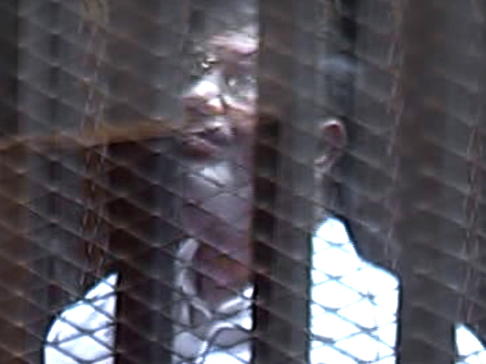 Former President Morsi stands inside a glass-encased metal cage in the Cairo courtroom
