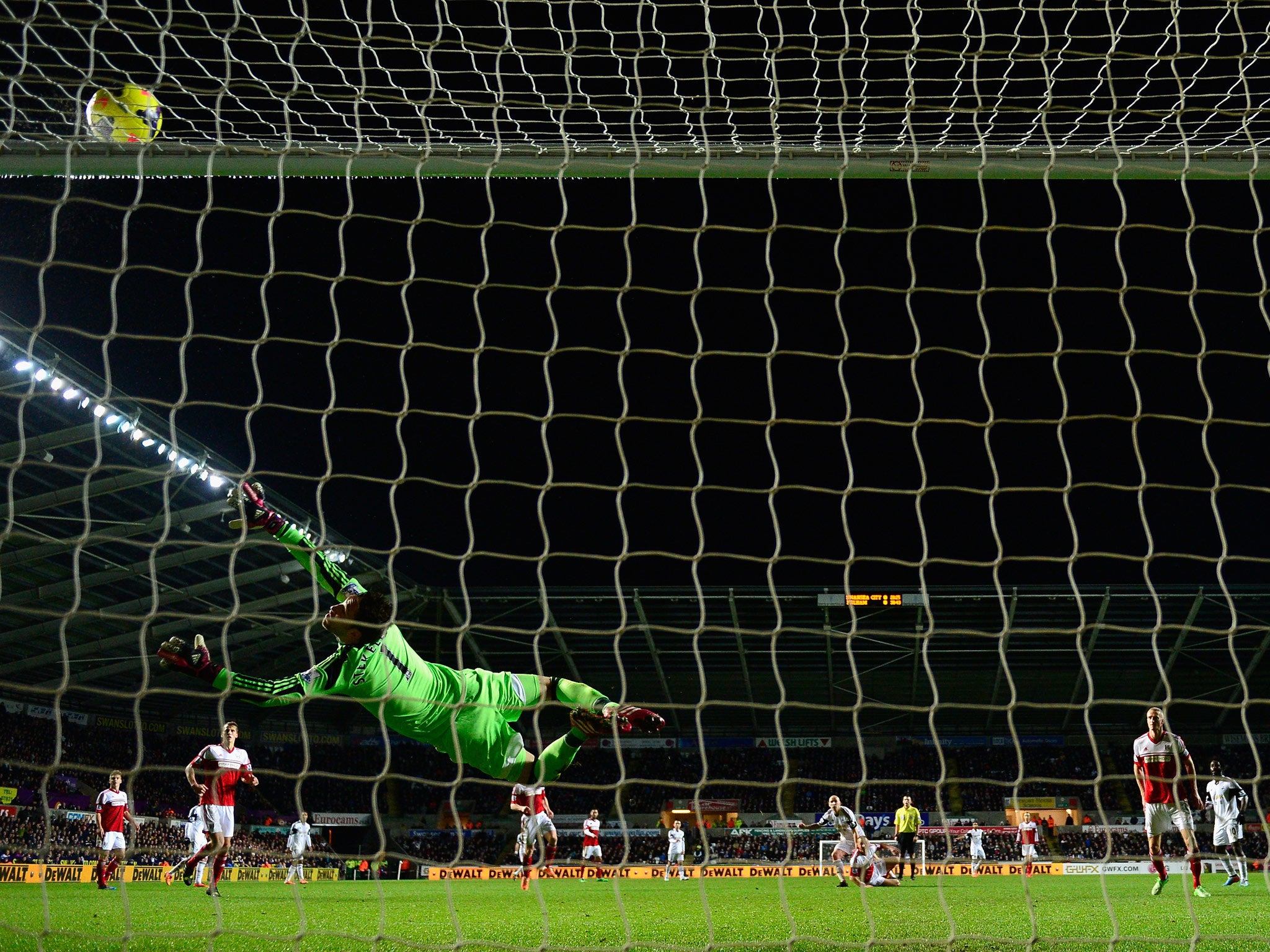 Fulham goalkeeper Maarten Stekelenburg dives in vain as a shot from Jonjo Shelvey (r) of Swansea strikes the bar