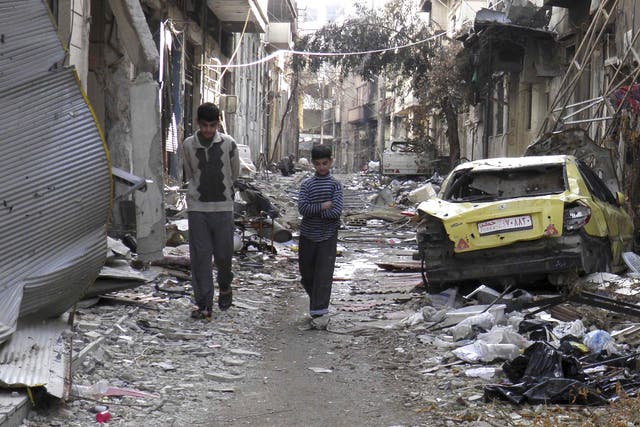 Boys walk along a street past damaged buildings and vehicles in the besieged area of Homs