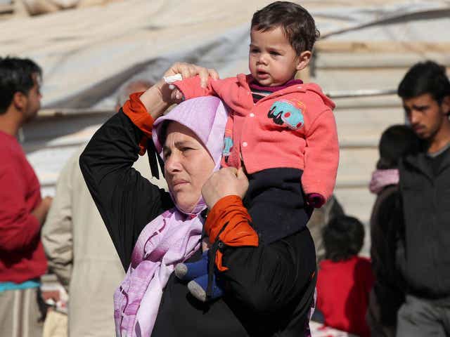 A Syrian woman carries a child on her shoulder at a refugee camp in Jordan