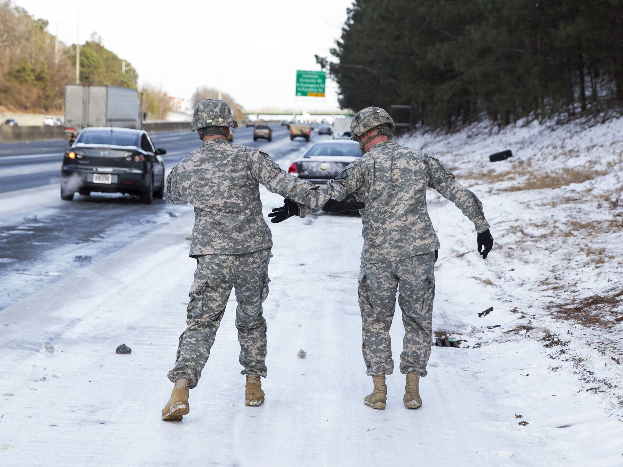 Georgia National Guard troops Command Sgt. Maj. Buddy Grisham (L) and Sgt. Chad Armstrong help each other from slipping on the ice as they assist people in getting their stranded cars out of the snow in Atlanta, Georgia January 29, 2014. A rare ice storm