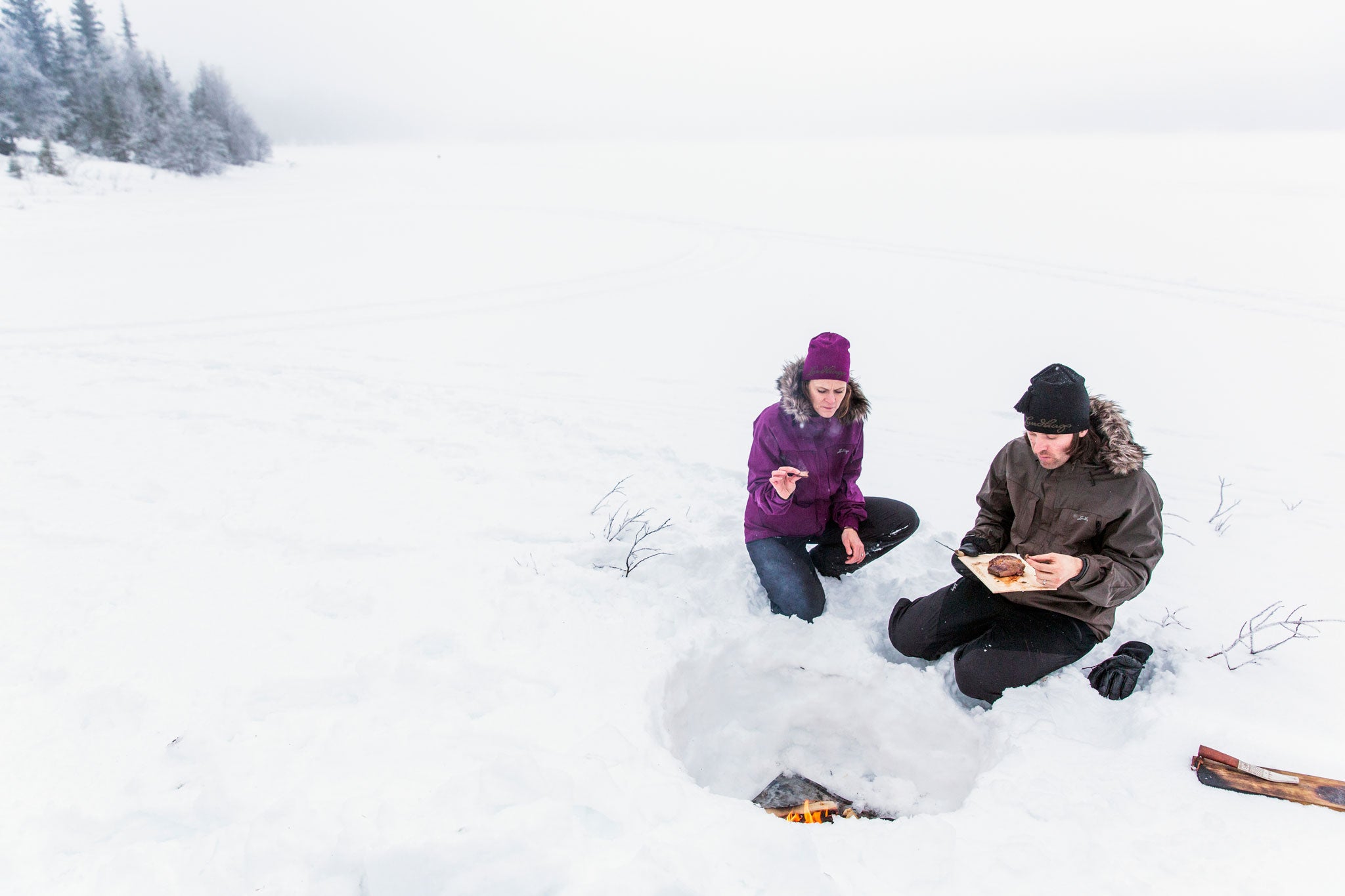 Susie Mesure and Niklas Ekstedt gather around the fire pit they have built in the snow