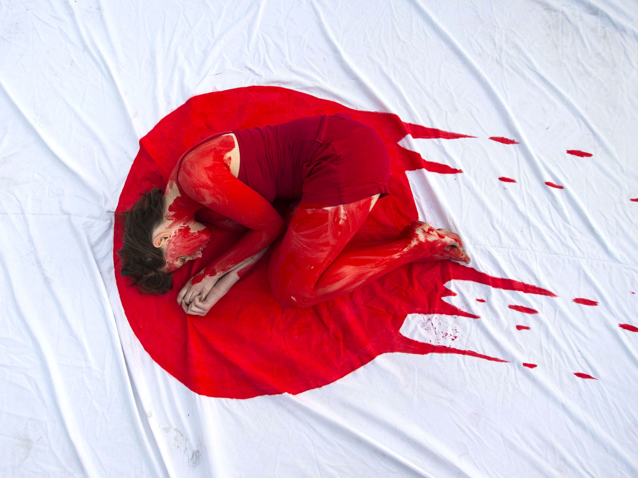 An member of the 'Taiji Dolphin Action Group' is curled up on a sheet depicting blood on the Japanese flag, during a protest against the killing of dolphins.