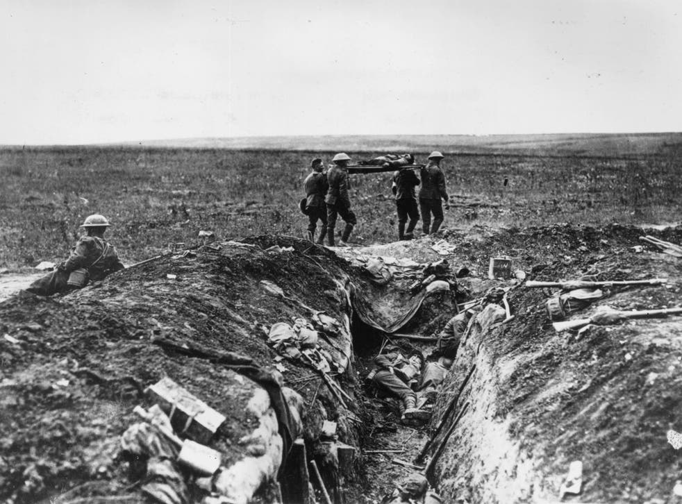 1915: A wounded British soldier is stretchered back to camp past a carnage-strewn trench, during the World War I
