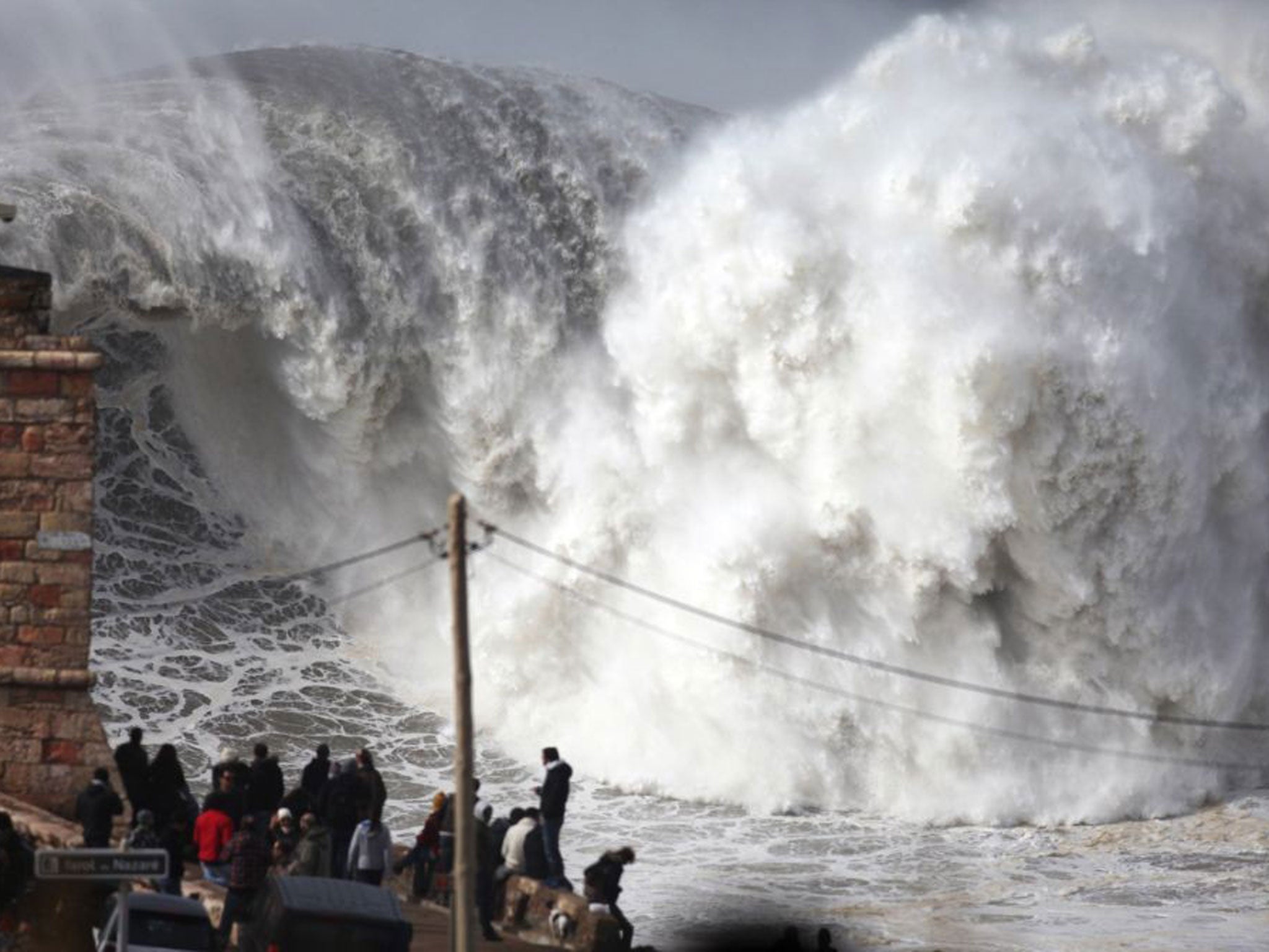 Spectators watch as huge waves crash into the beach.