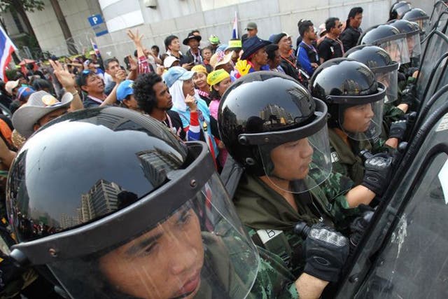 Thai soldiers stand guard to block anti-government protesters (left) during a rally outside the office of the permanent secretary for defense where Prime Minister Yingluck Shinawatra was reportedly working inside