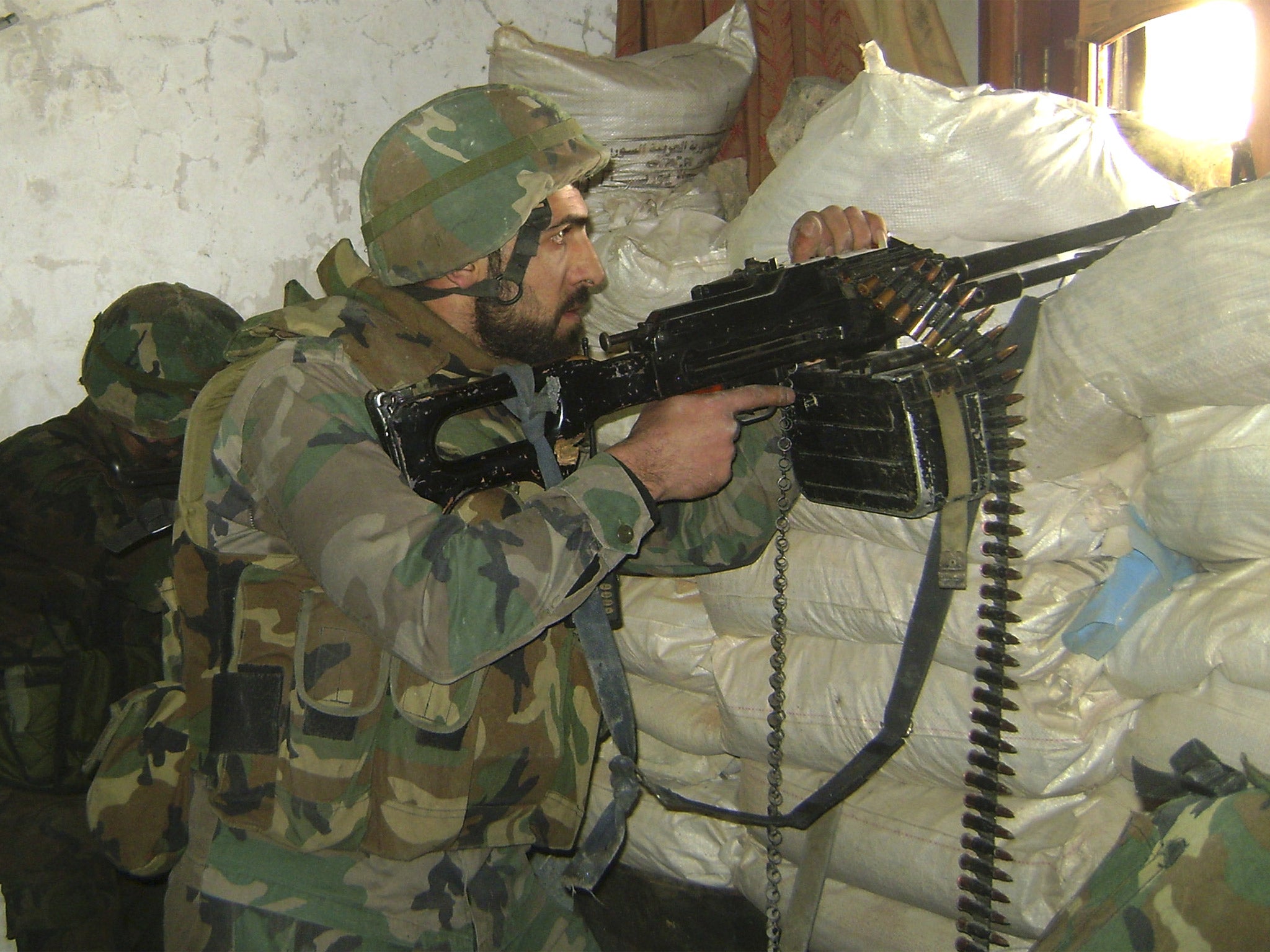 A Syrian army soldier takes his position behind sand barriers, in Homs