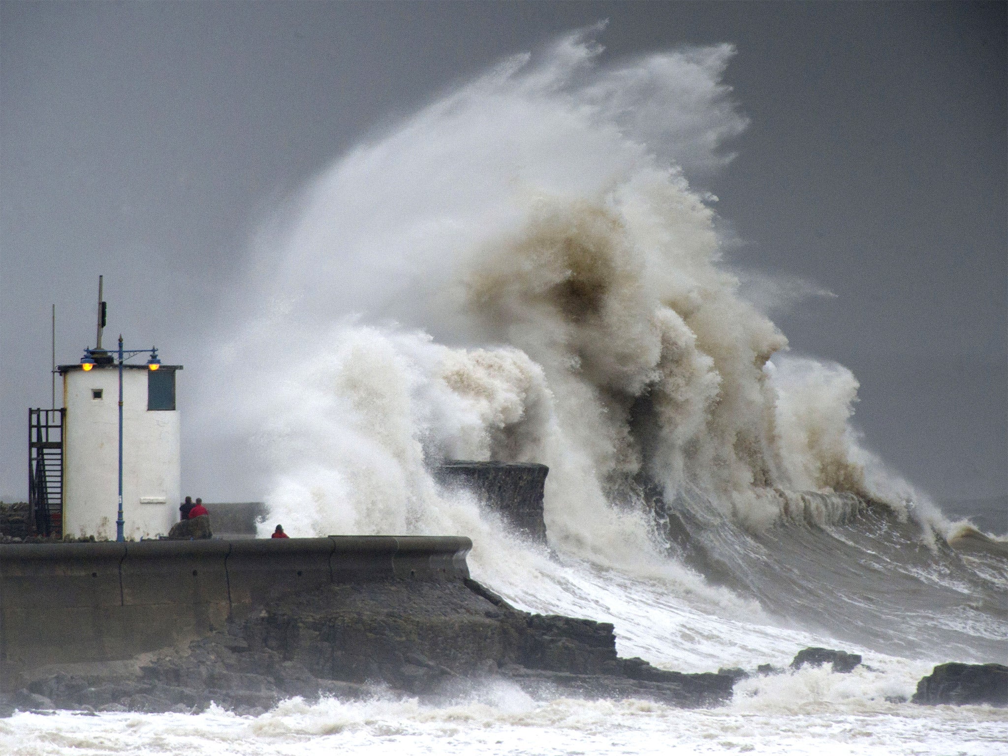 Spectators watch as waves break over the harbour wall at Porthcawl, Wales, during a high tide