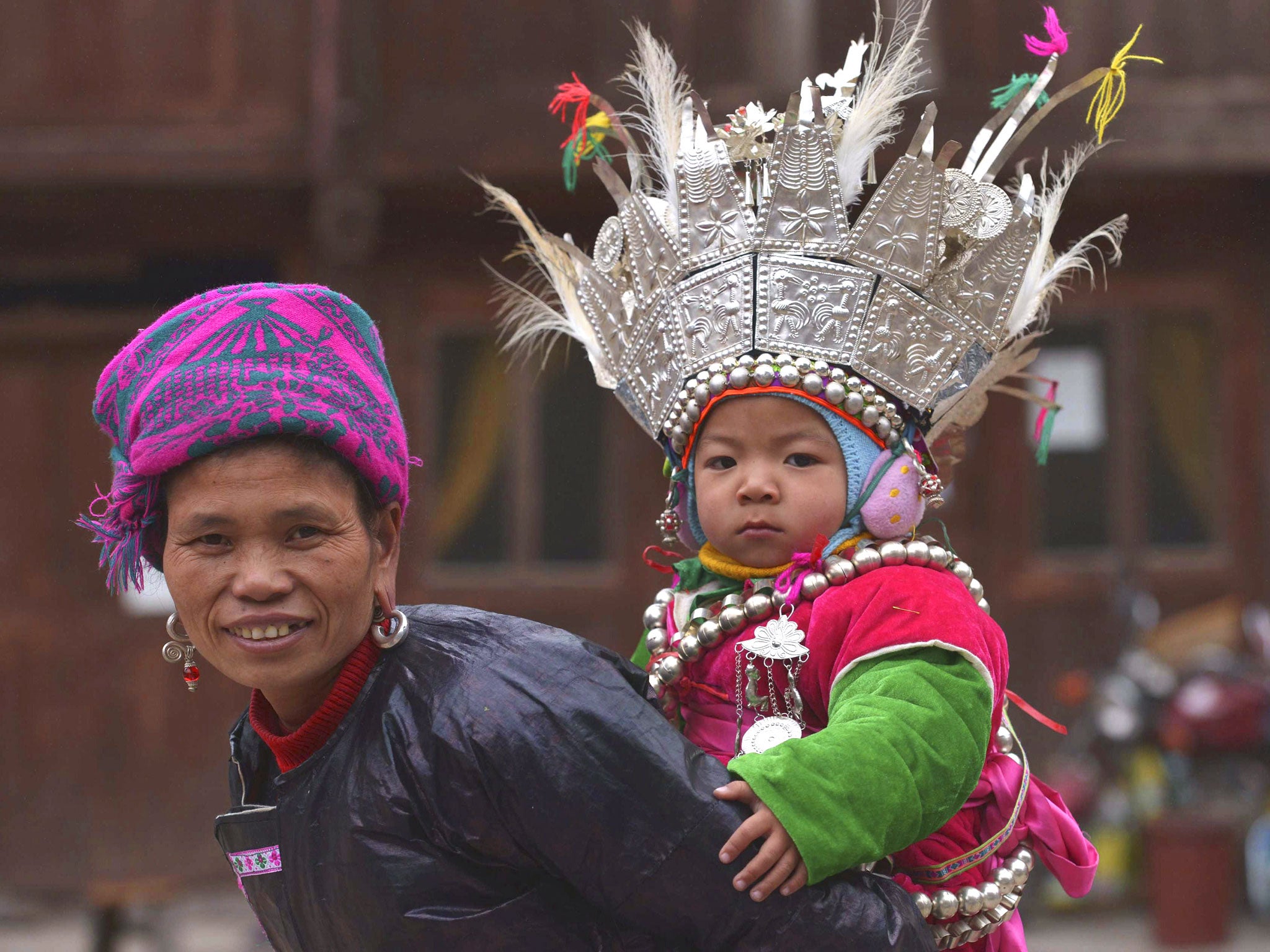 An ethnic Dong Minority woman in traditional costume carries a child on her back during a performance to celebrate the traditional Dong Minority festival 'Tai Guan Ren' in Huanggang village of Liping county, Guizhou province