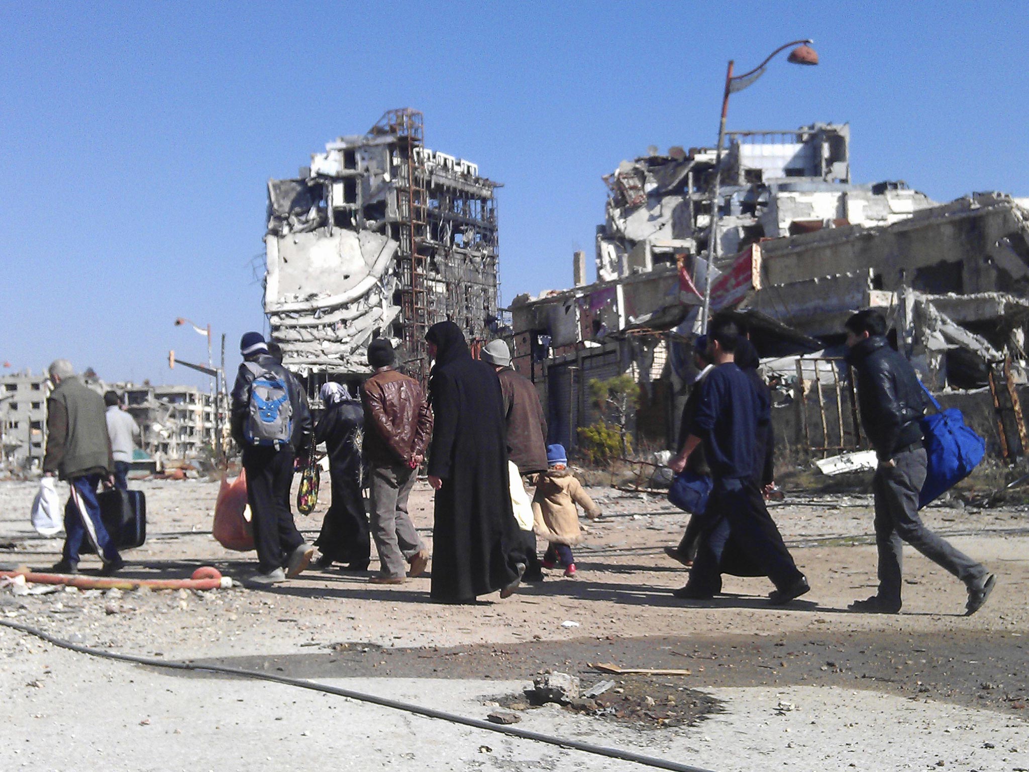 Civilians carry their belongings as they walk towards a meeting point to be evacuated from a besieged area of Homs