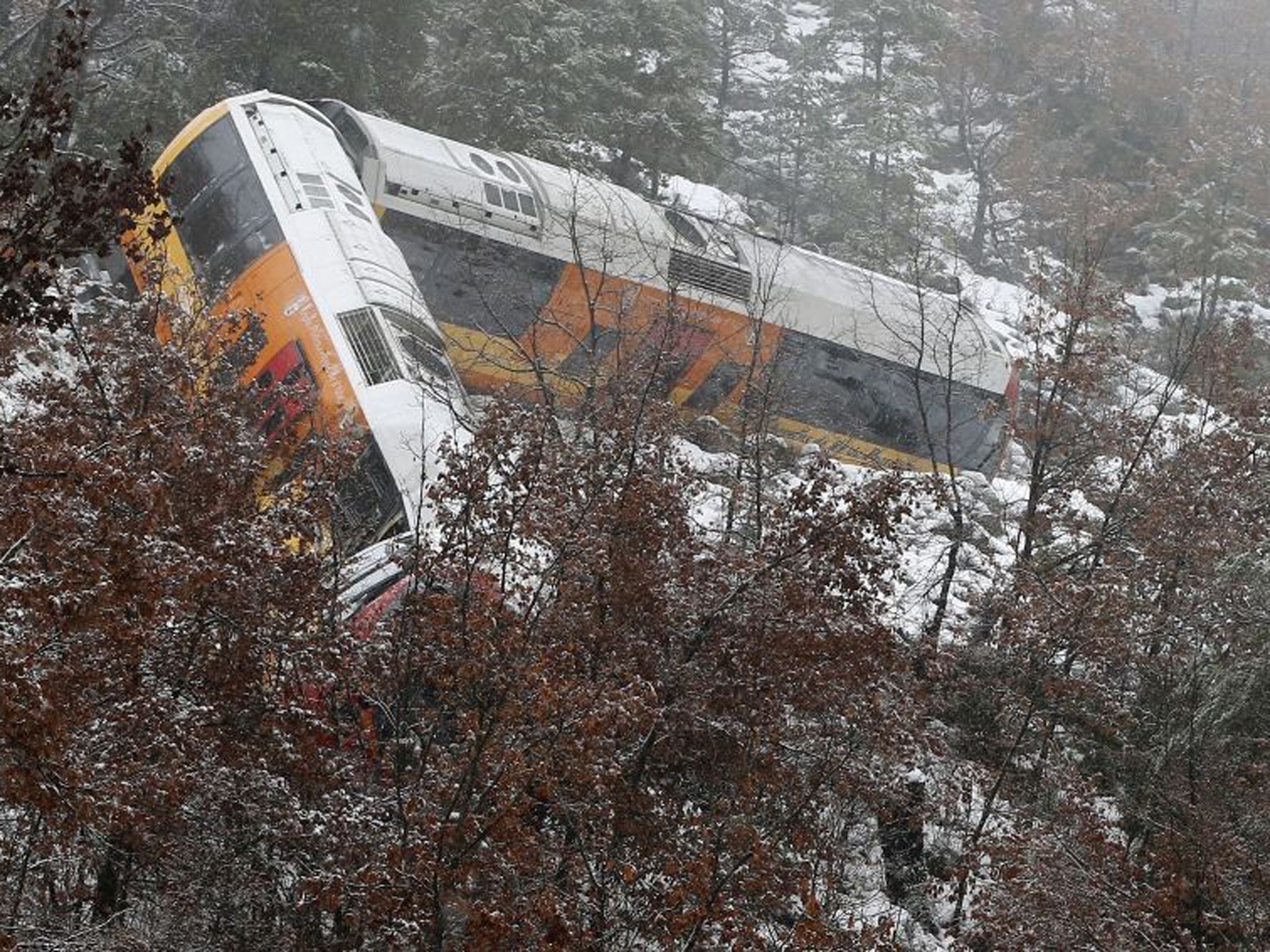 The train hangs from a ledge after it had been derailed by a boulder