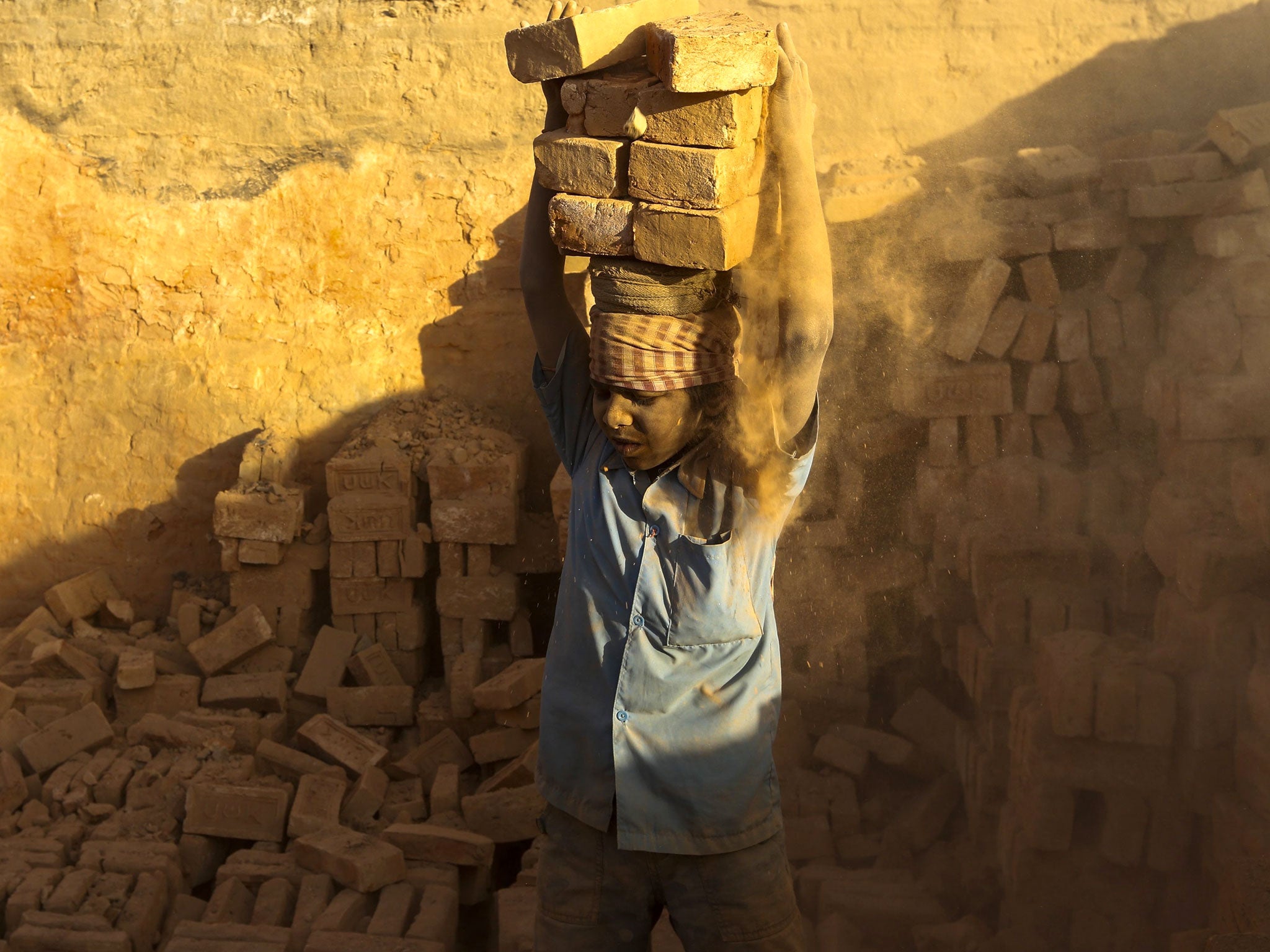 A young boy lifts heavy bricks as he works at brick factory around Kathmandu valley
