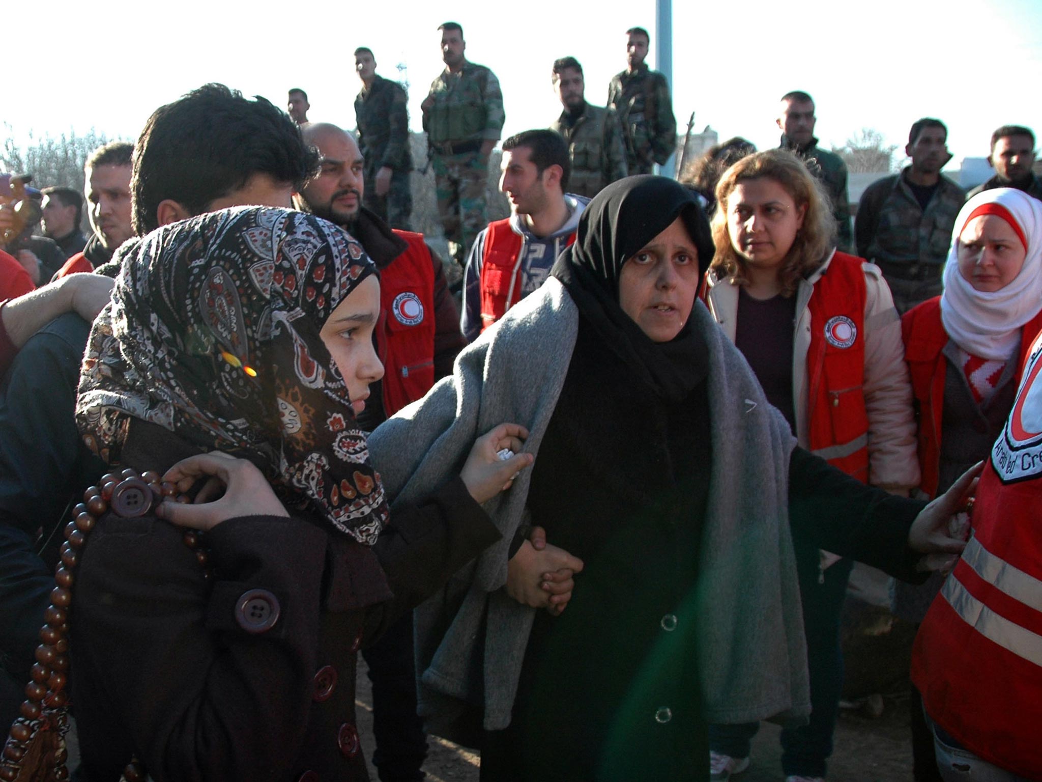 Two women walk towards a bus to evacuate the battleground city of Homs, Syria