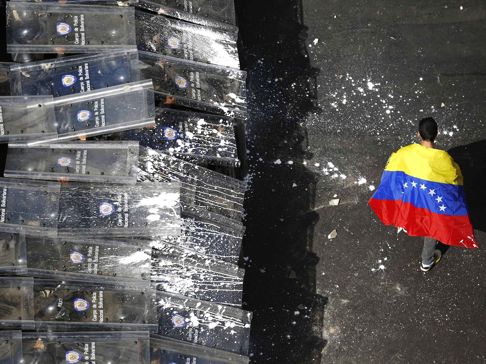 A demonstrator with a Venezuelan flag draped around himself protests against the government of Venezuela's President Nicolas Maduro, in front of a riot police line in Caracas