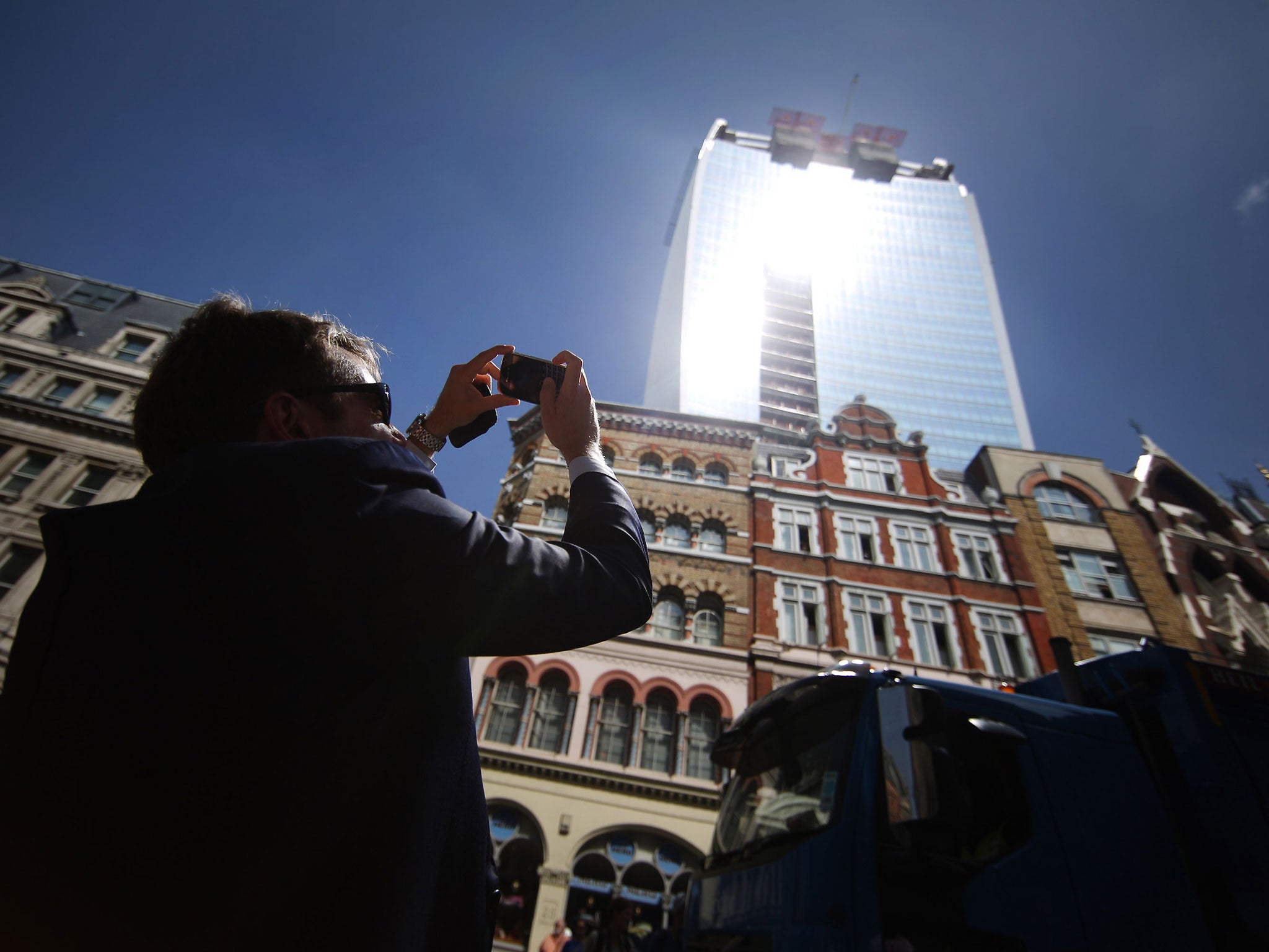 A man takes a photograph as the sun glares down from the Walkie Talkie building.