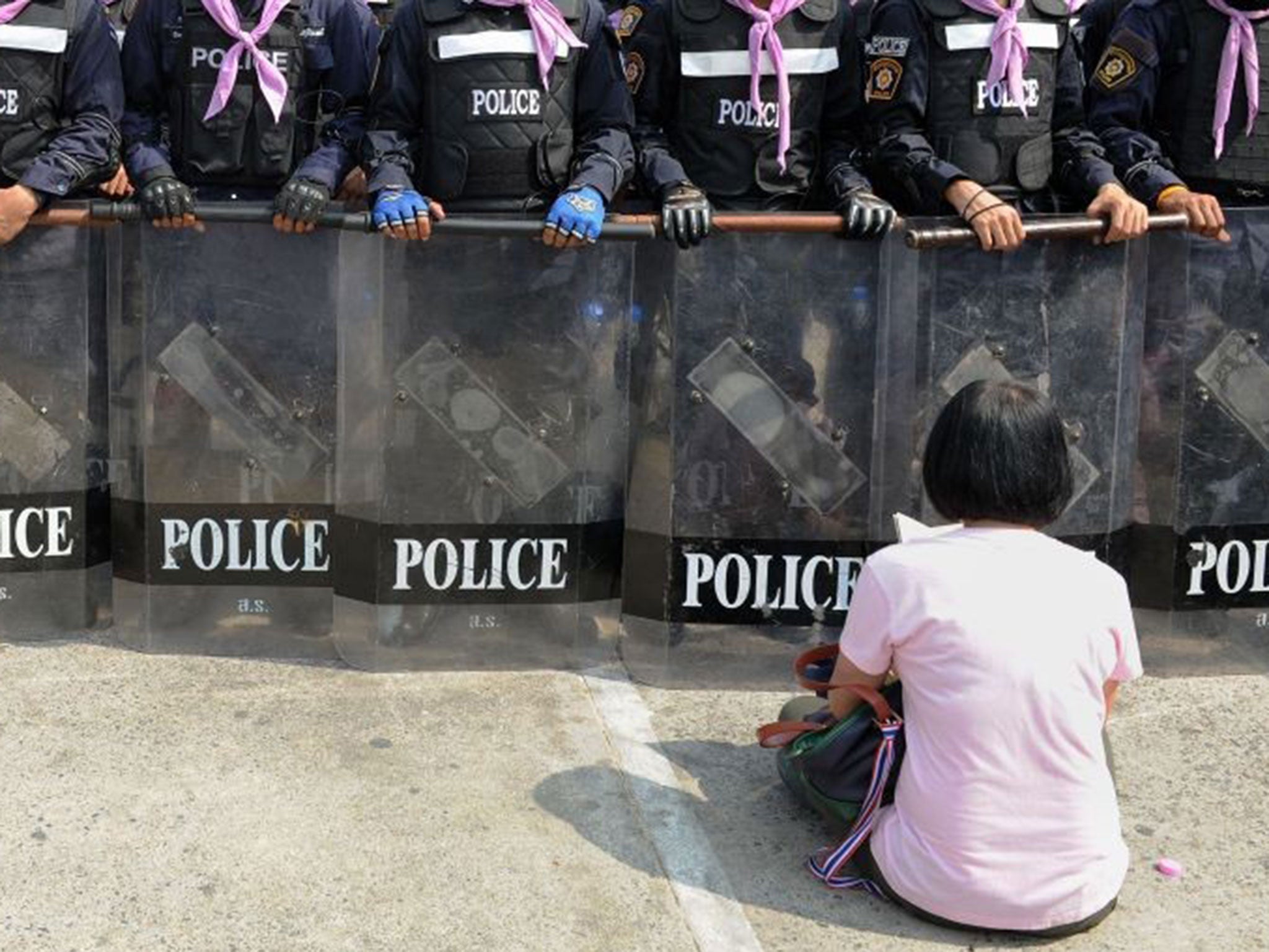 An anti-government protester sits in front of a group of police officers and reads from a Bhuddhist prayer book near the Government House building in Bangkok