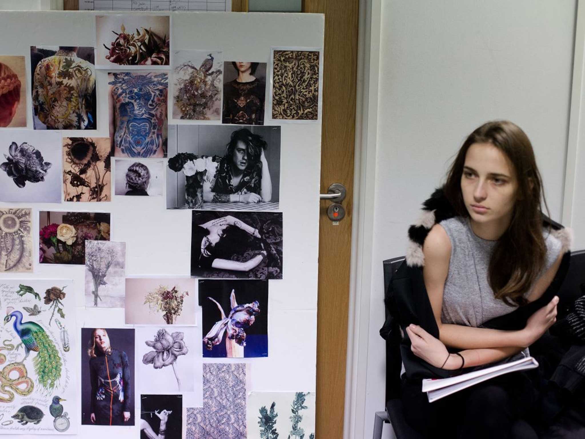 A model waits next to a moodboard for the show