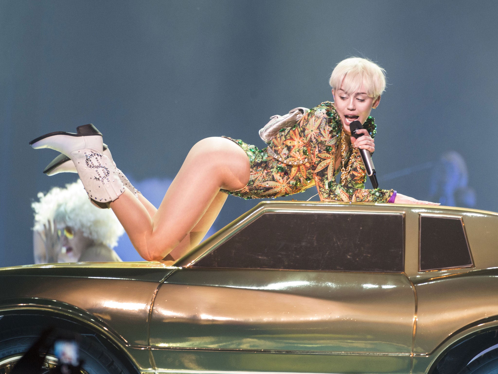Miley wore white boots with dollar signs on as she cavorted around on a gold car