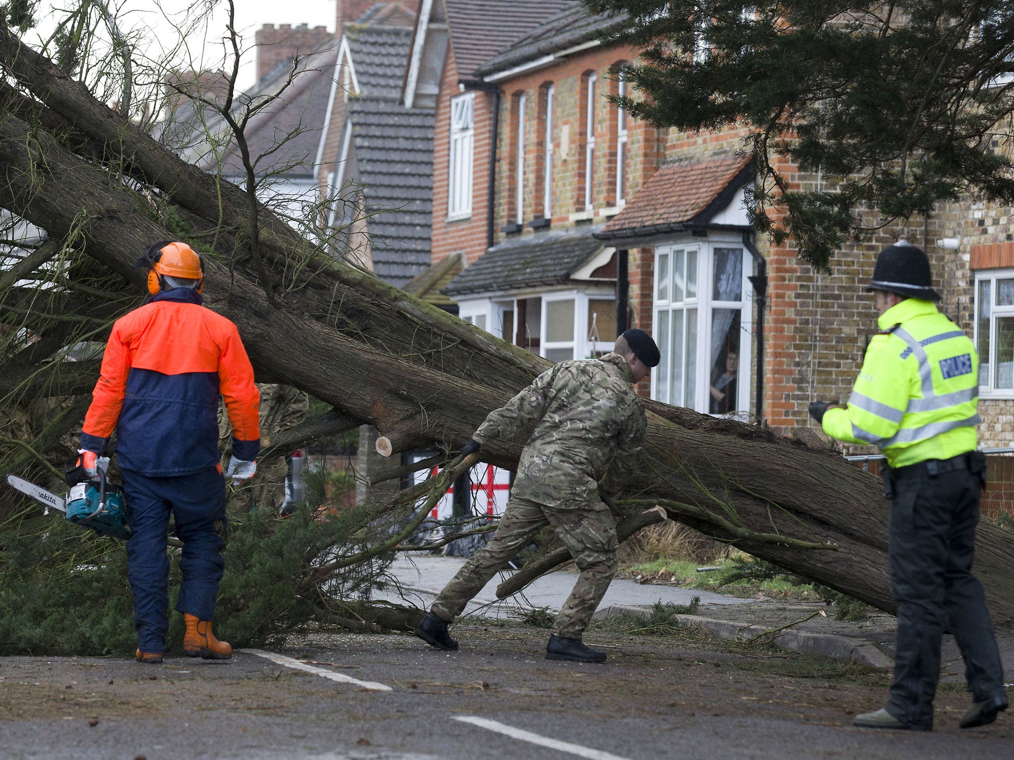 A police officer looks on as a British solider helps a tree surgeon remove a fallen tree in Egham, west of London after high winds brought by a winter storm battered southern England