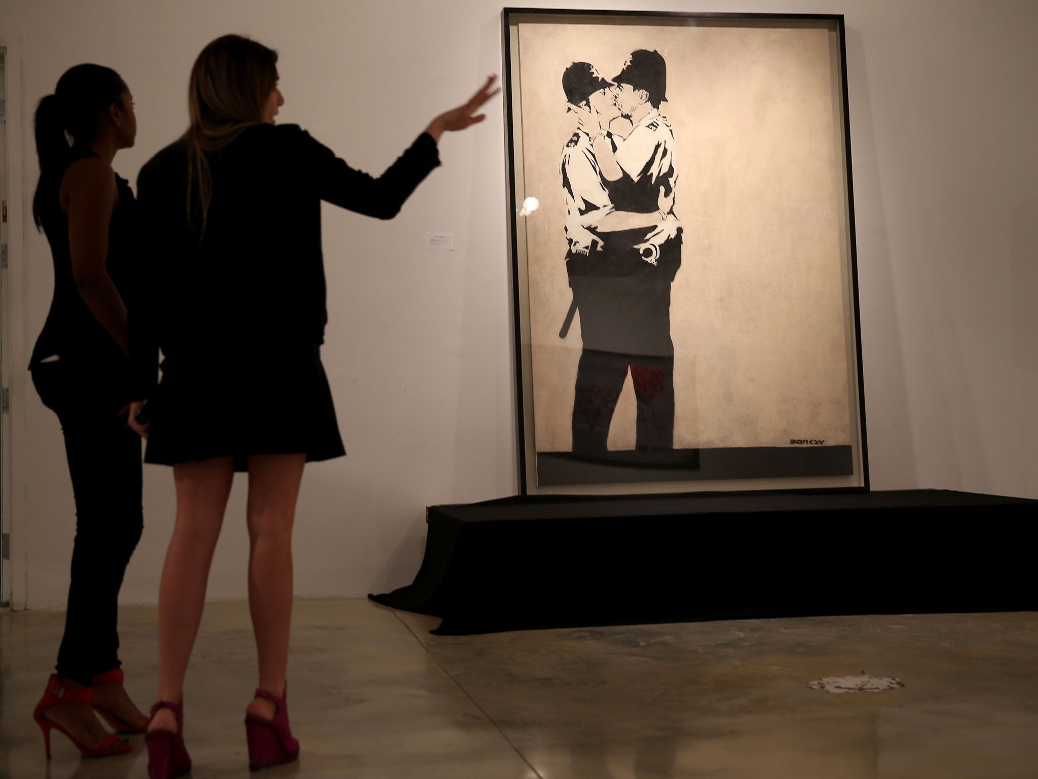 People stand in front of Banksy's 'Kissing Coppers' before it sold for $575,000 at auction in Miami