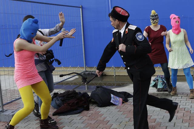 A Cossack militiaman attacks Nadezhda Tolokonnikova and a photographer as she and fellow members of the punk group Pussy Riot, including Maria Alekhina, right, in the pink balaclava, stage a protest performance in Sochi, Russia, on Wednesday, Feb. 19, 201