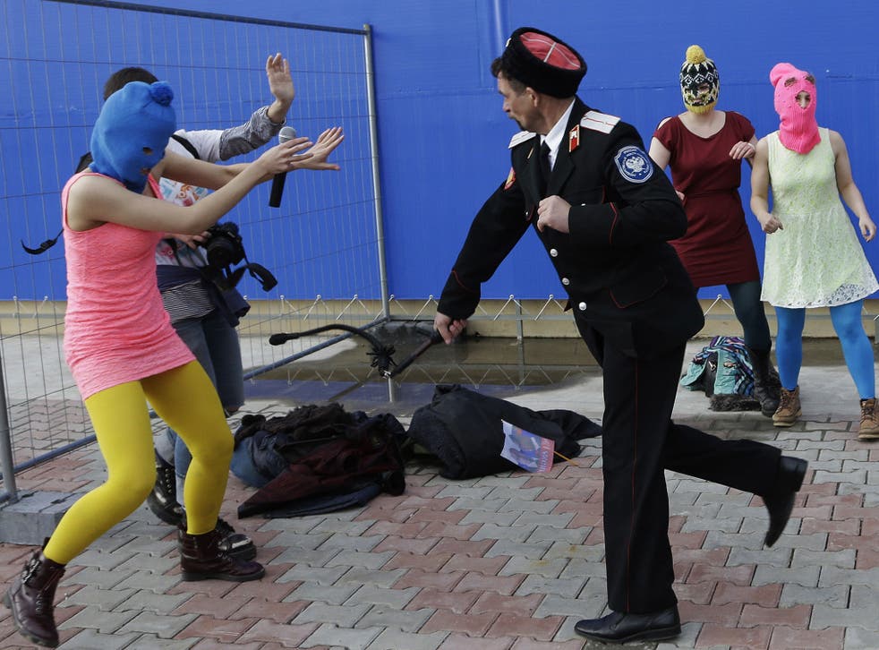 A Cossack militiaman attacks Nadezhda Tolokonnikova and a photographer as she and fellow members of the punk group Pussy Riot, including Maria Alekhina, right, in the pink balaclava, stage a protest performance in Sochi, Russia, on Wednesday, Feb. 19, 201
