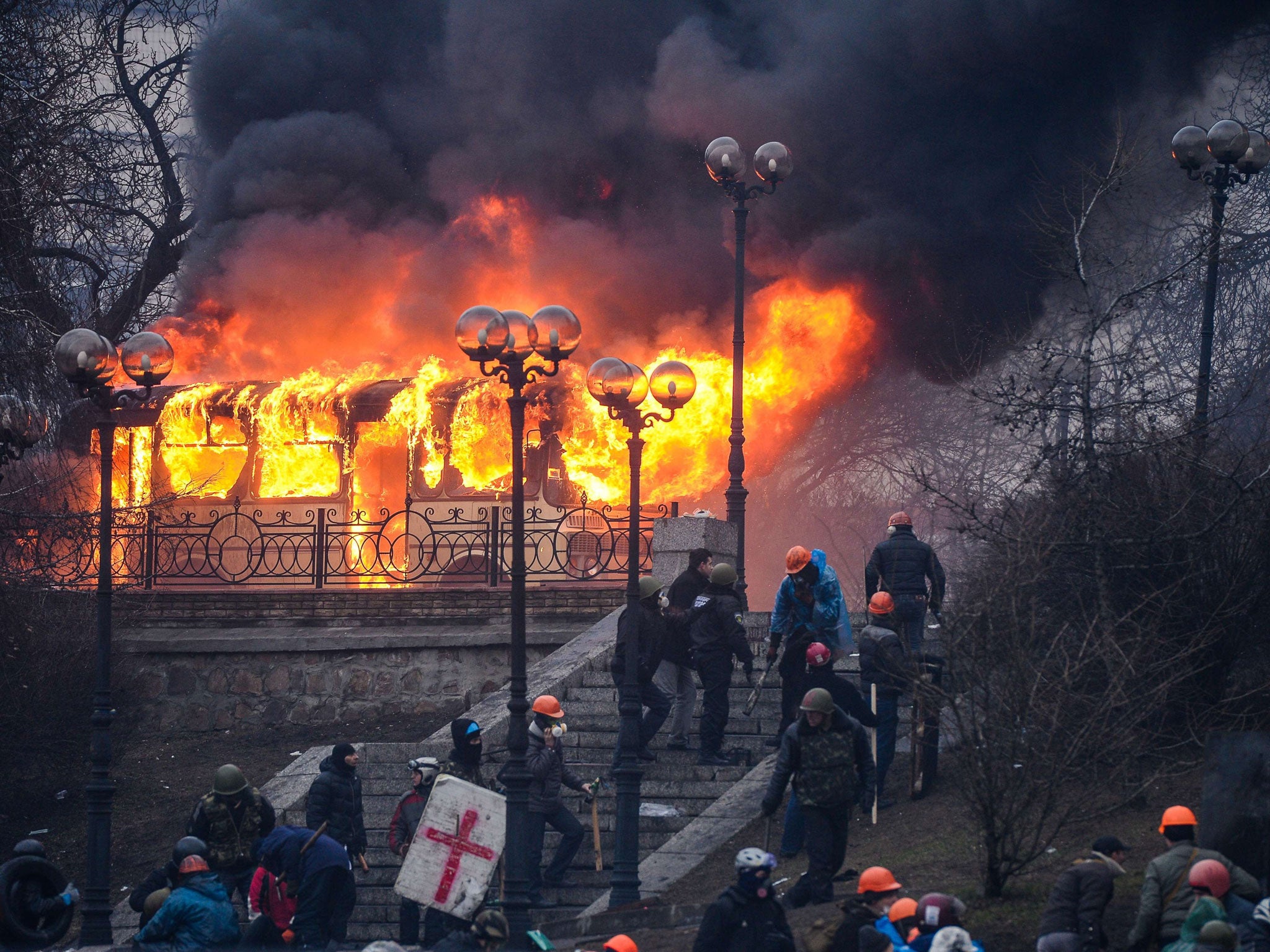 Protesters walk and stand near a burning bus at the Institutskaya Street close to the central Independence Square in Kiev (Getty Images)