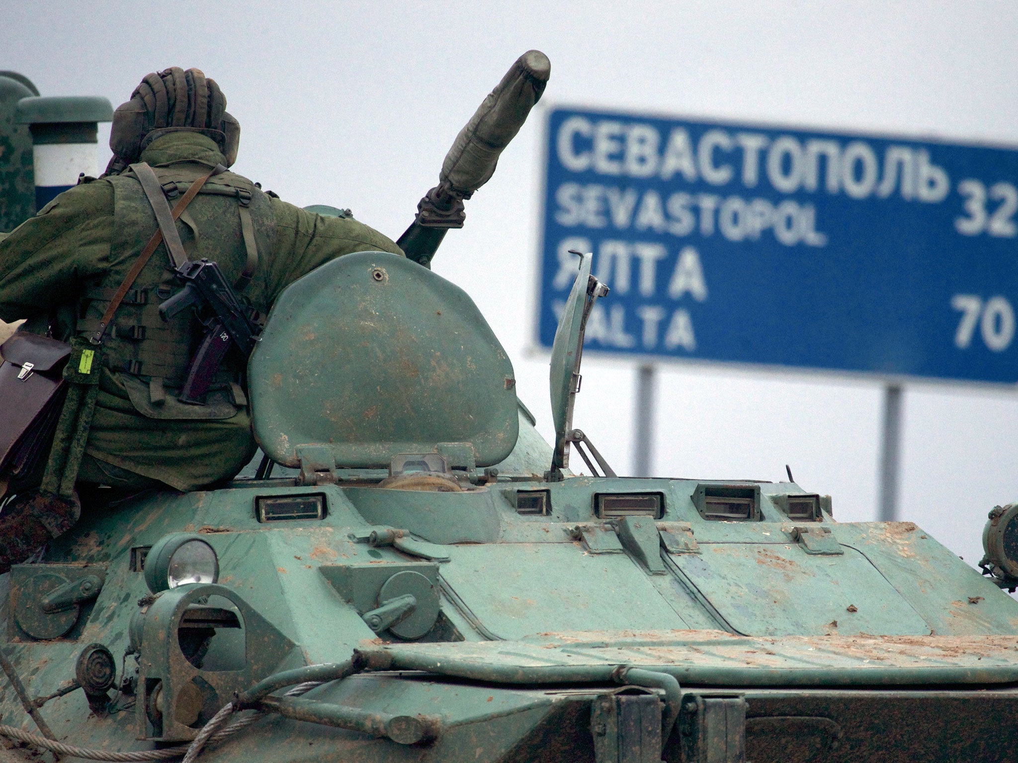 A soldier rests atop a Russian armored personnel carriers with a road sign reading "Sevastopol - 32 kilometers"