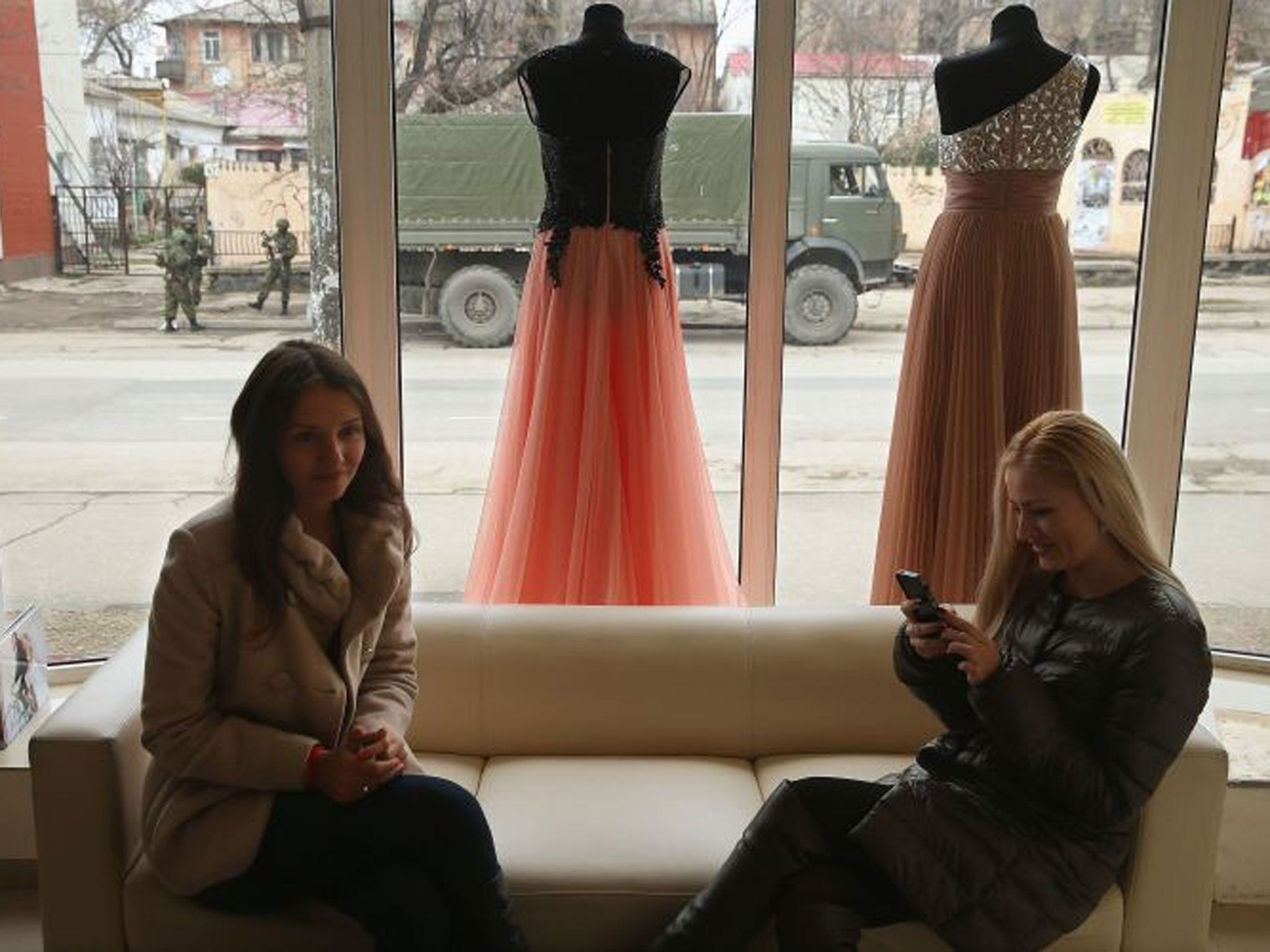 Two women sit in an evening gown shop as soldiers stand in the streets of Simferopol