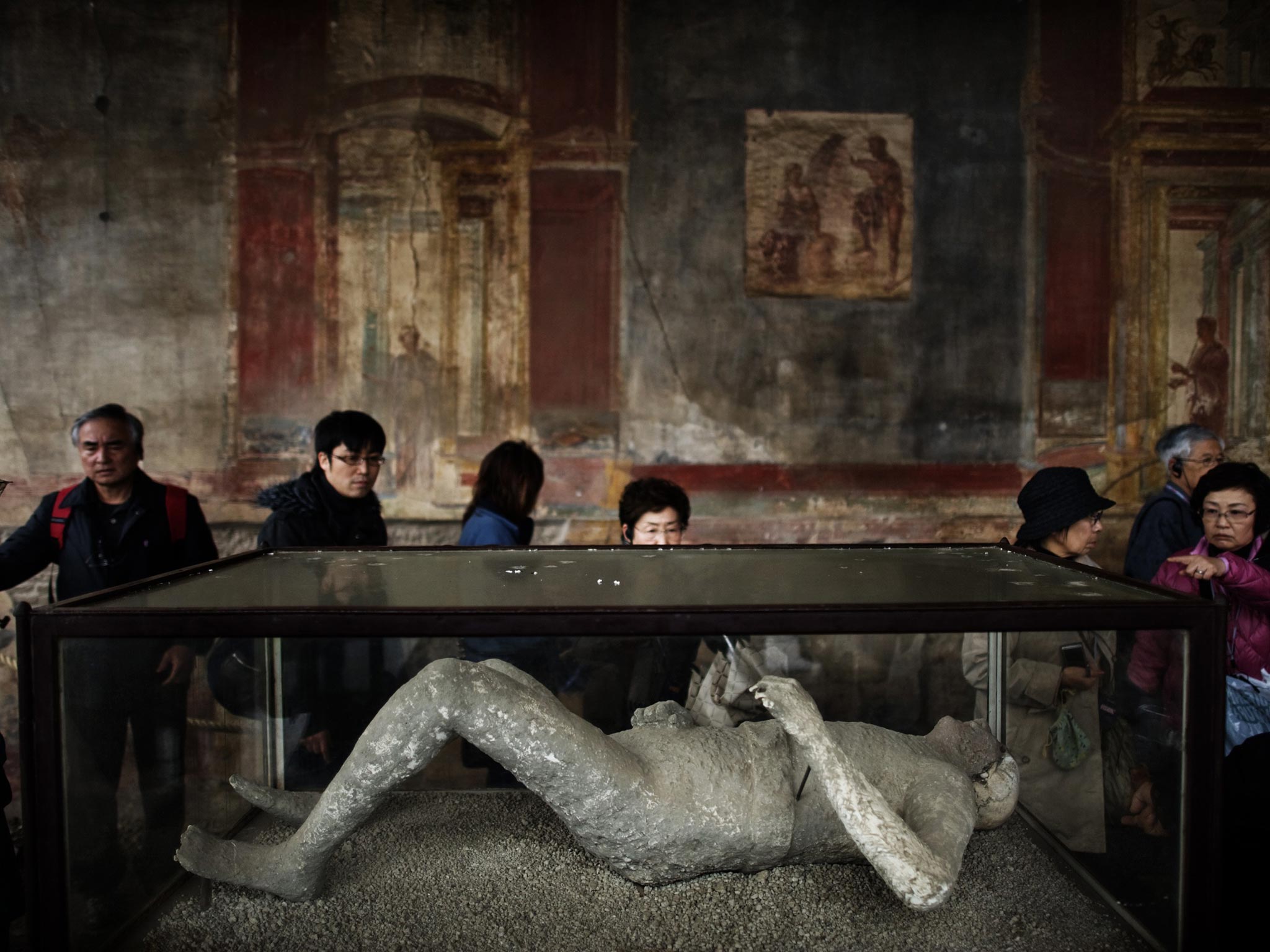 Tourists look at a body cast during their visit the archeological site of Pompeii