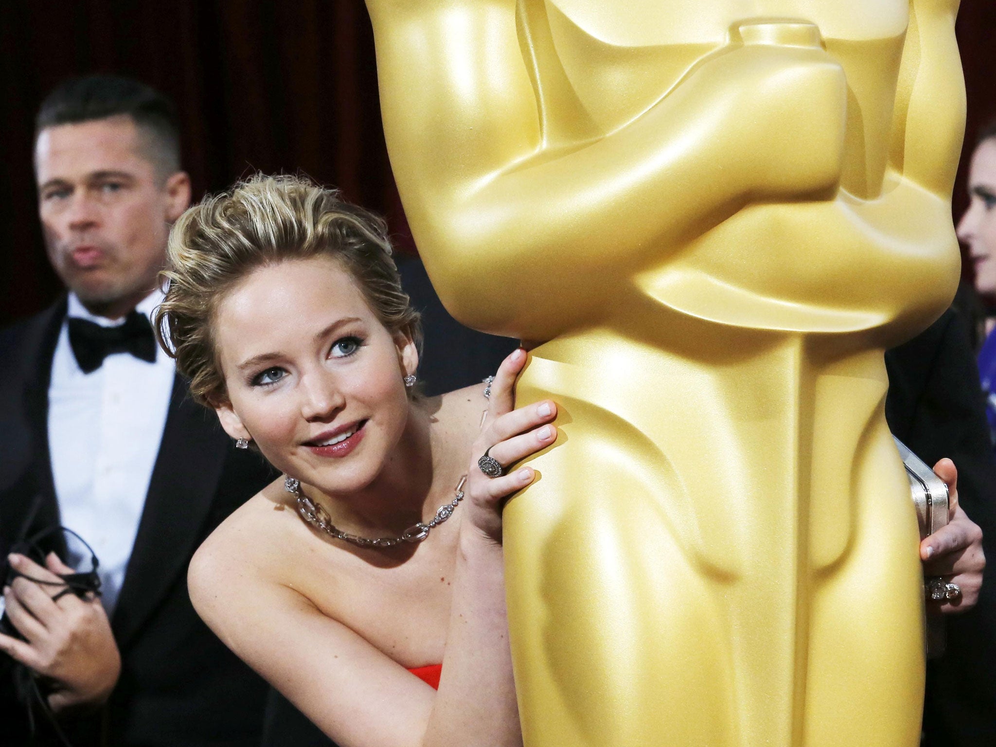 Jennifer Lawrence, best supporting actress nominee for her role in the film 'American Hustle', peeks around an Oscar statue on the red carpet as actor Brad Pitt (L) looks on at the 86th Academy Awards in Hollywood