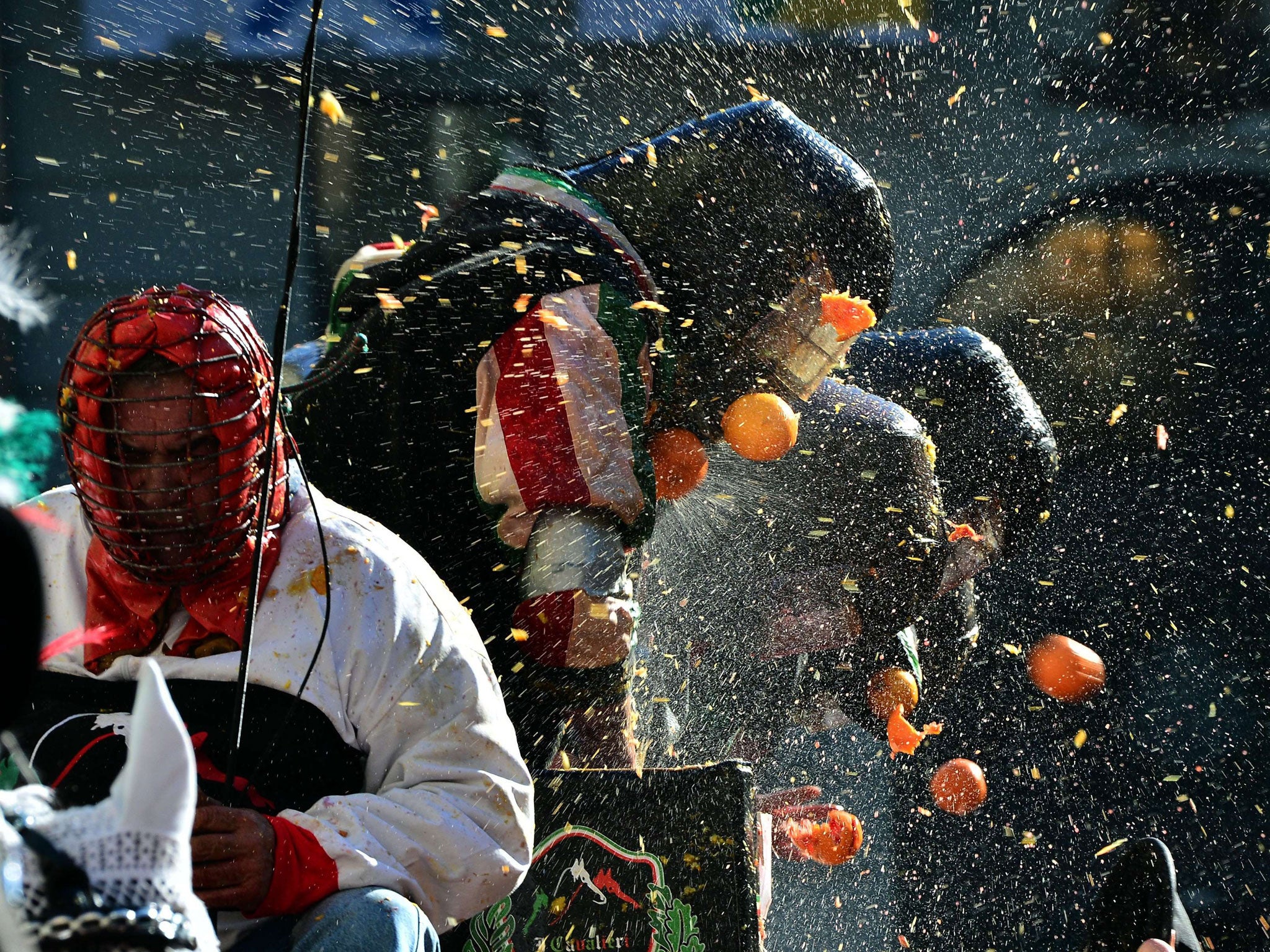 Men with helmets are hit by oranges during the traditional 'battle of the oranges' held during the carnival in Ivrea, near Turin