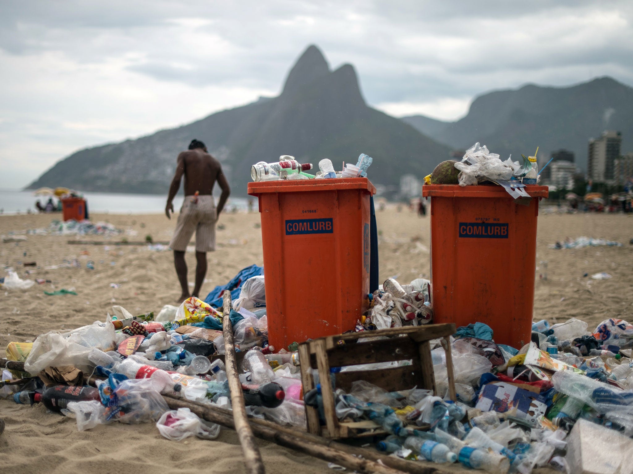 A man walks next to full trash cans on Ipanema beach.