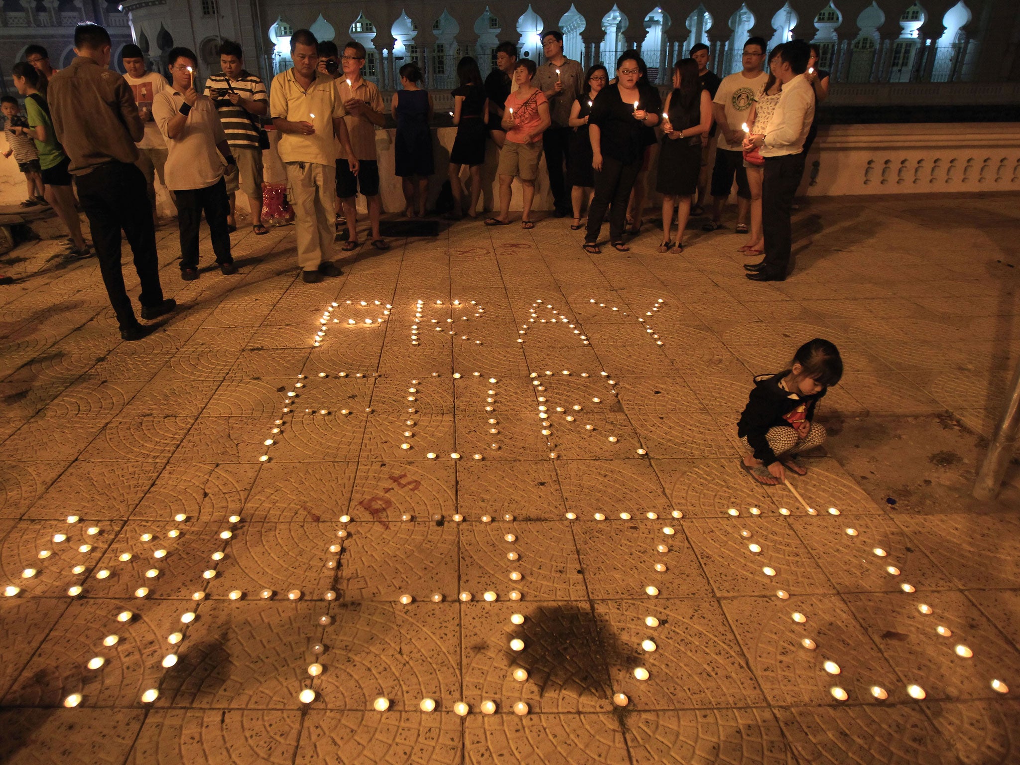 A girl lights a candle next to a message reading 'Pray for MH370' during a candlelight vigil for passengers of the Malaysia Airlines flight