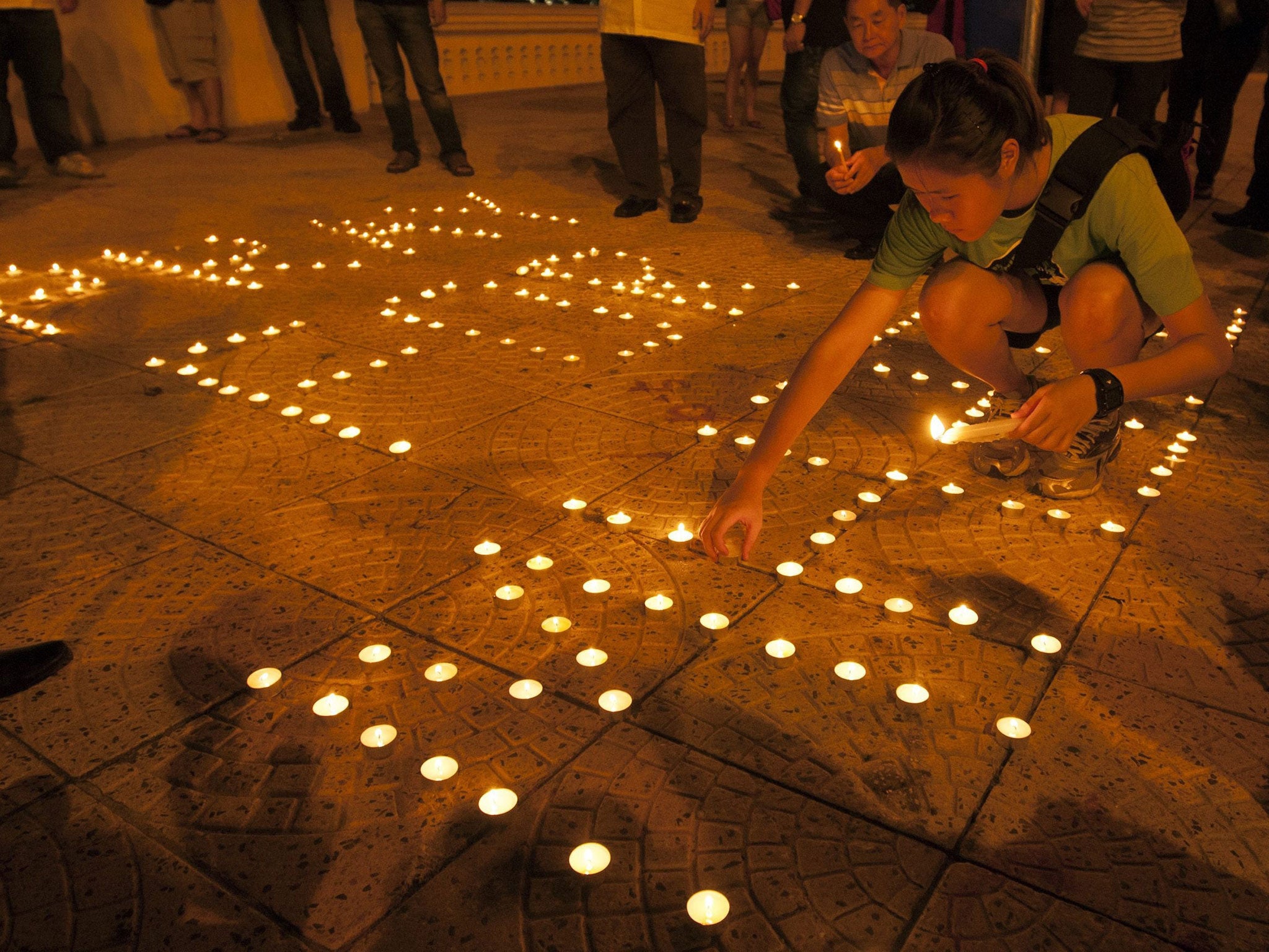 A girl places a candle to form a slogan during a vigil for the missing Malaysia Airlines passengers (EPA)