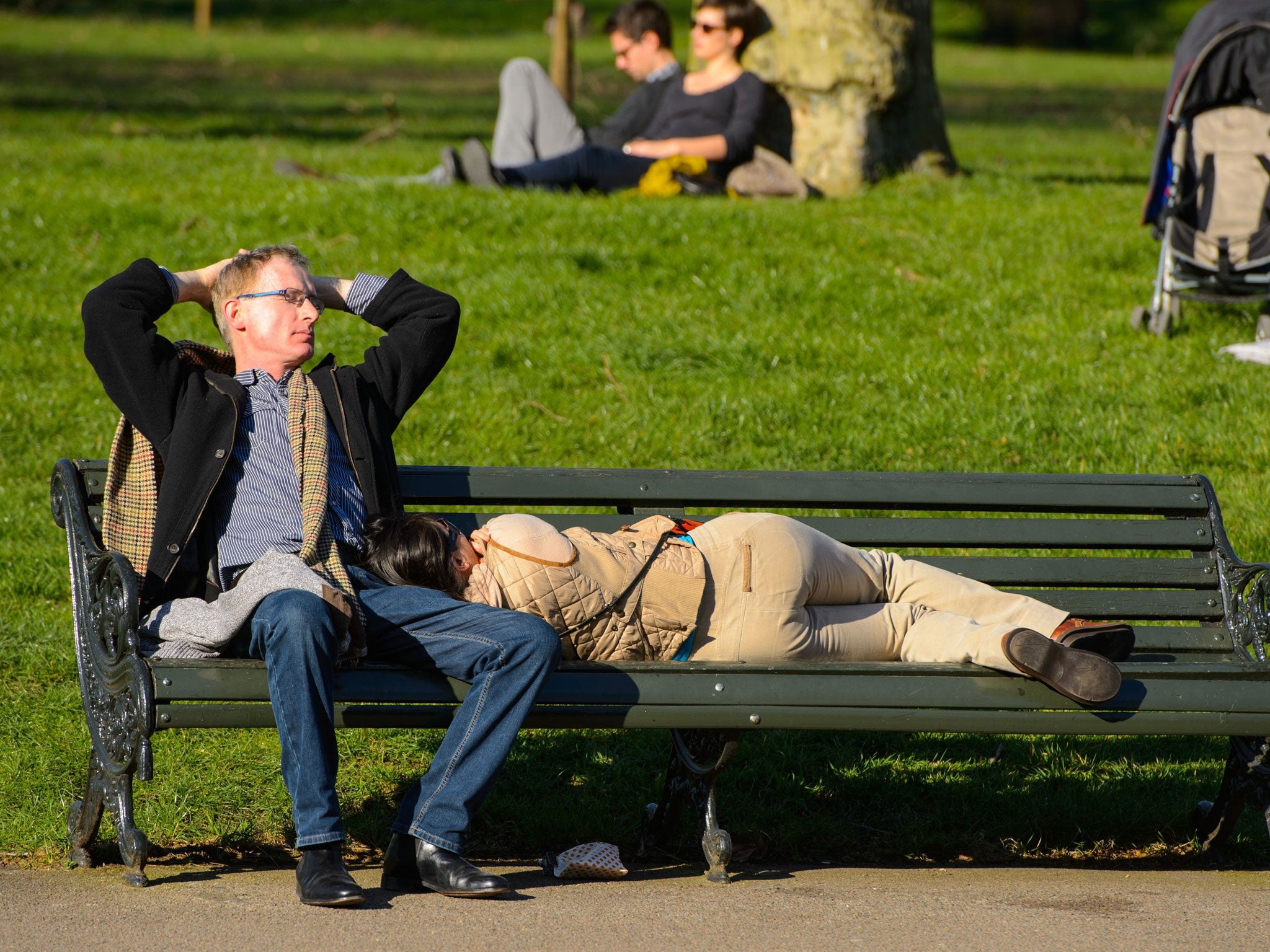 People sleep in the sun on a bench as they enjoy the weather in Hyde Park, central London