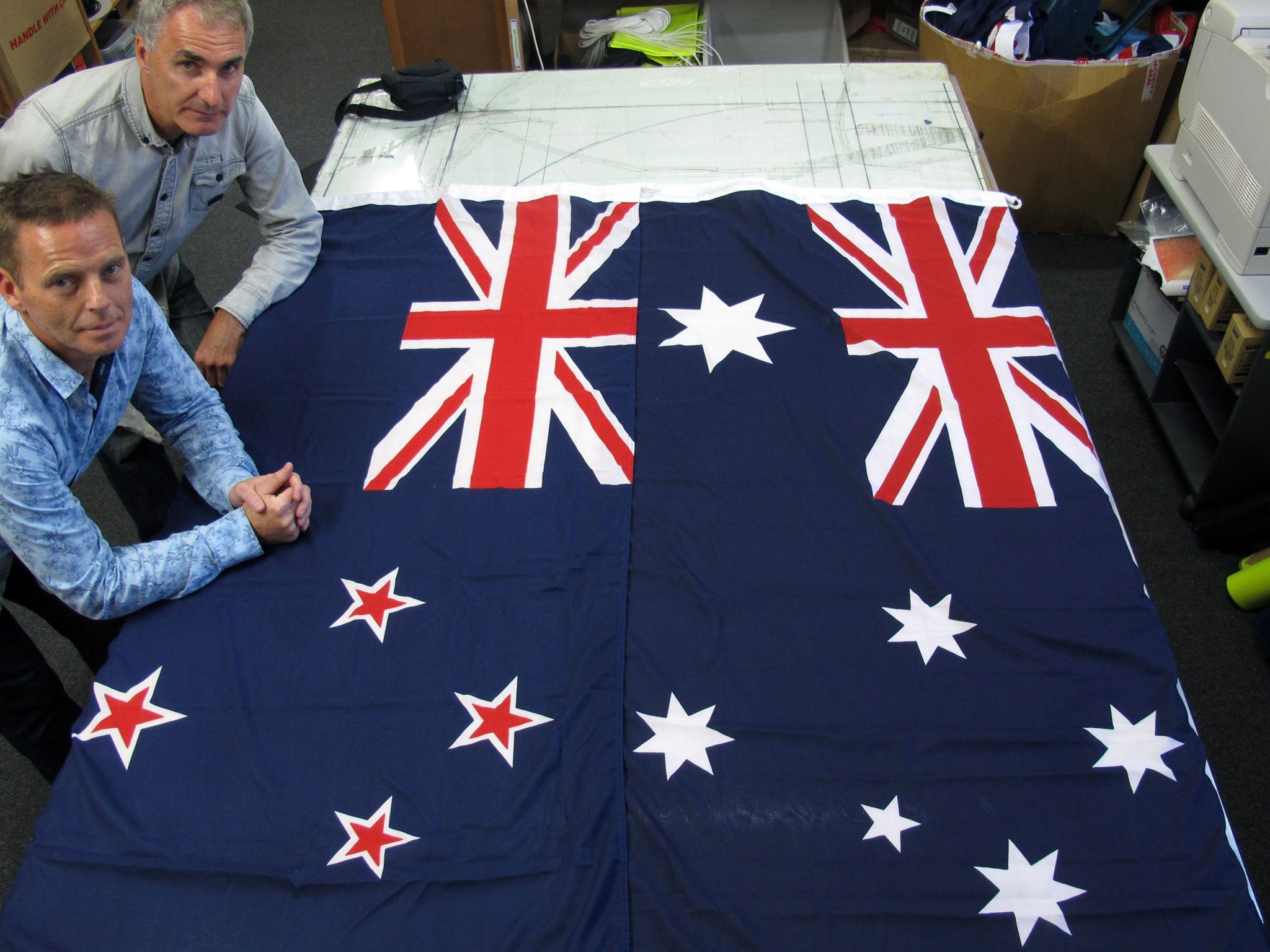 David Moginie, managers at flag manufacturer Flagmakers, pose next to flags of New Zealand, left, and Australia, in their factory near Wellington, New Zealand. New Zealanders will get to vote soon on whether to change their national flag, which many view