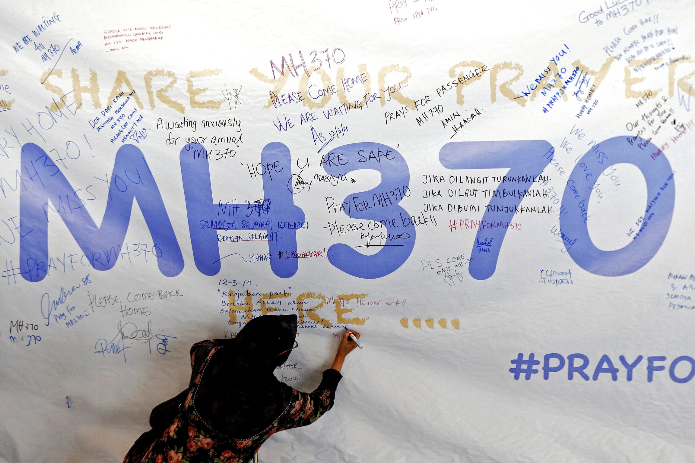 A woman writes a message of support and hope for the passengers of the missing Malaysia Airlines MH370 on a banner at Kuala Lumpur International Airport