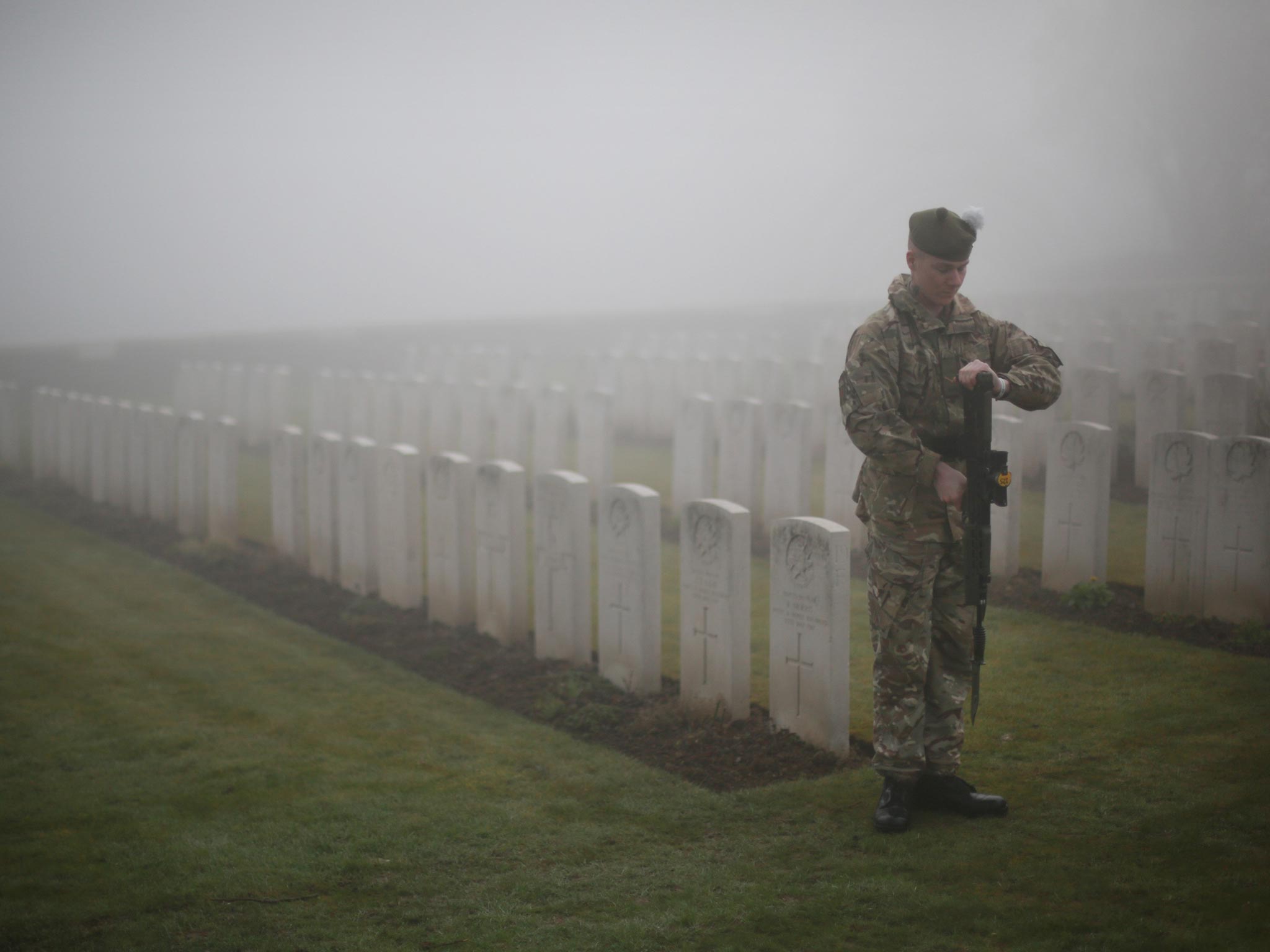 A soldier of The 2nd Battalion The Royal Regiment of Scotland presents arms amongst World War One headstones