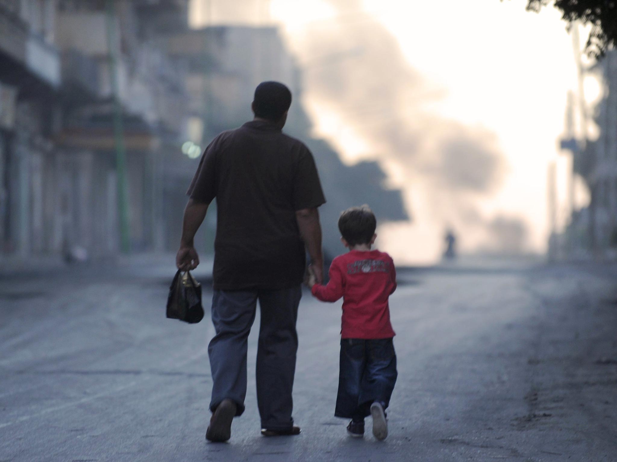 A Syrian man walks with his son along a deserted street in the town of Maarat al-Numan