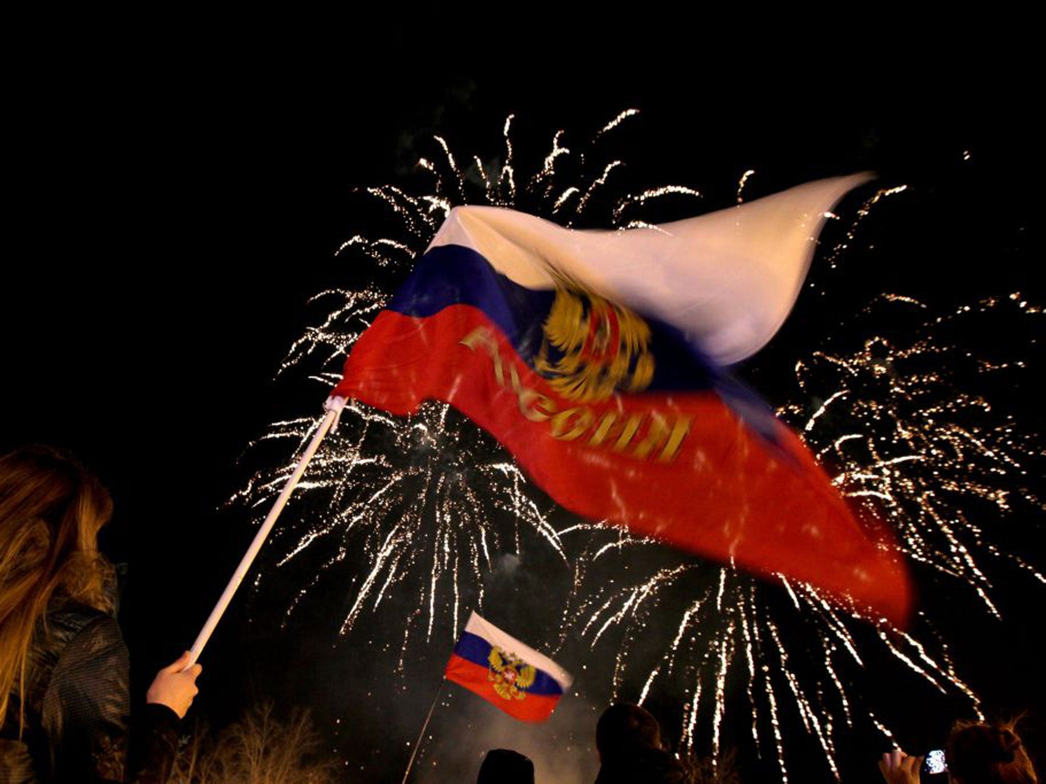 People wave Russian flags as fireworks explode in the sky over Sevastopol following the announcement of the result of the referendum