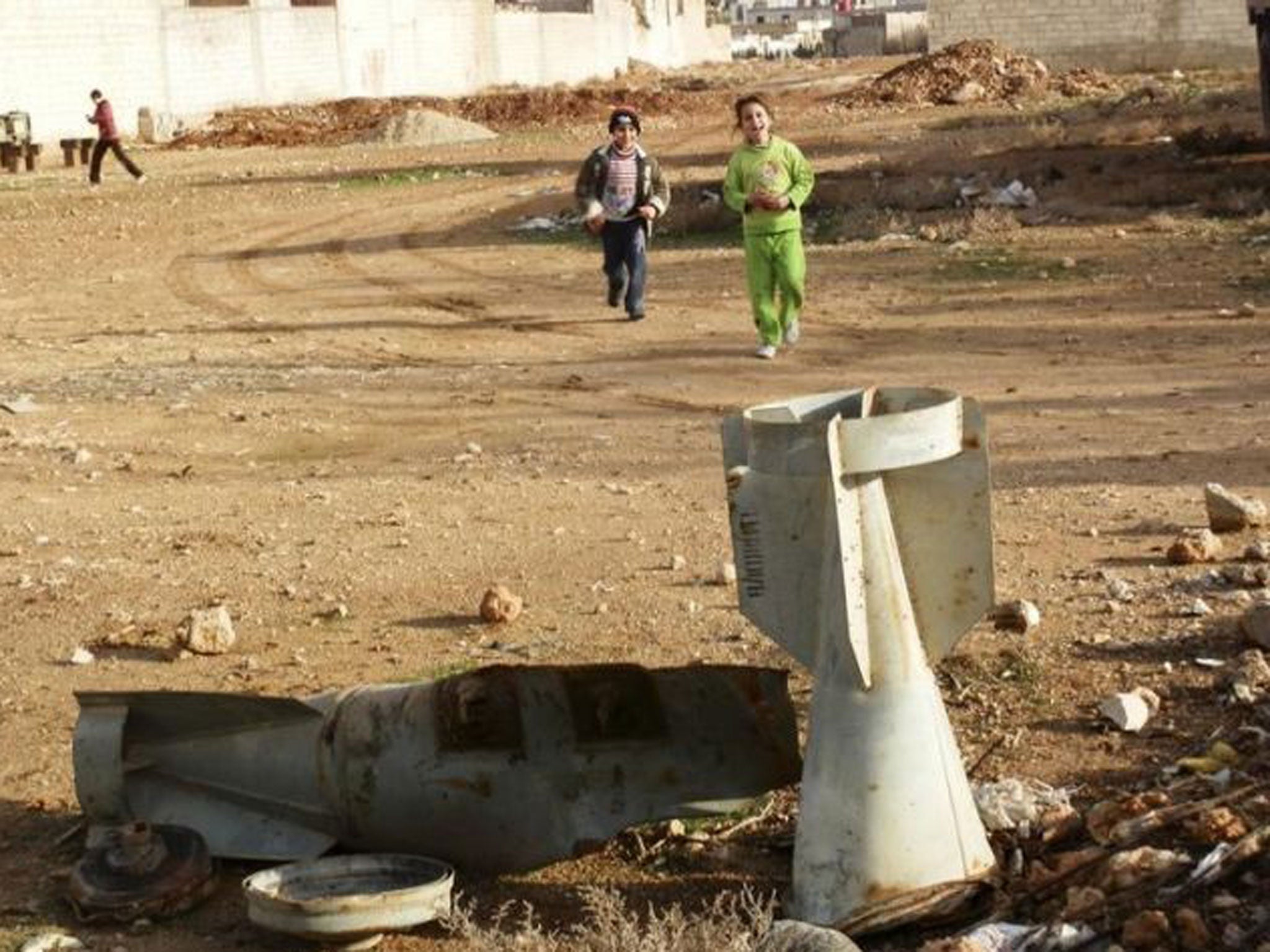 Children play near the remnants of a bomb shell in the ground, which activists said were fired by a Syrian Air Force fighter jet loyal to Syria's President Bashar al-Assad, in Daraya