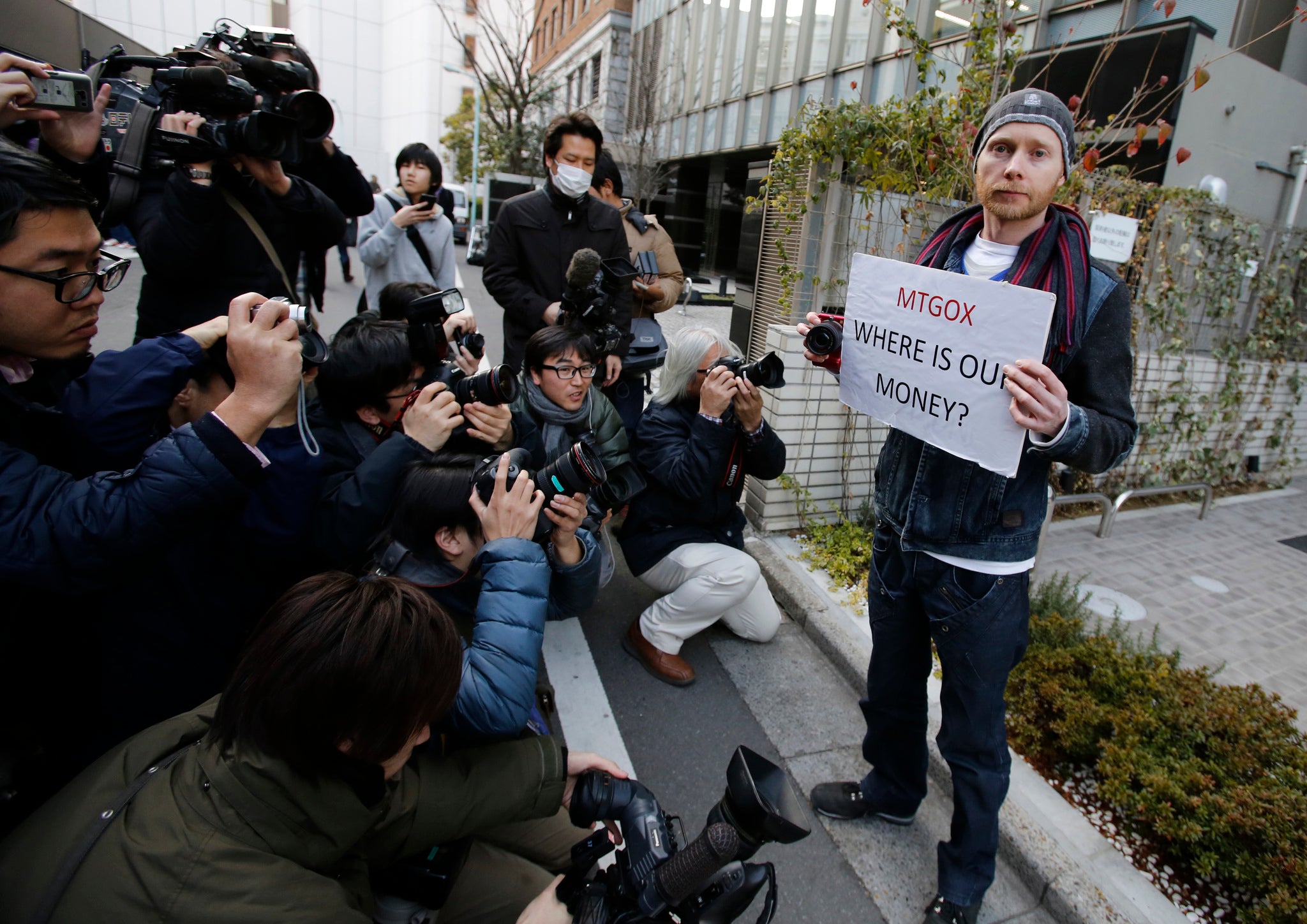Kolin Burges (R), a self-styled cryptocurrency trader and former software engineer from London, holds a placard to protest against Mt. Gox, as photographers take photos of him in front of the building where the digital marketplace operator was formerly housed in Tokyo February 26, 2014.