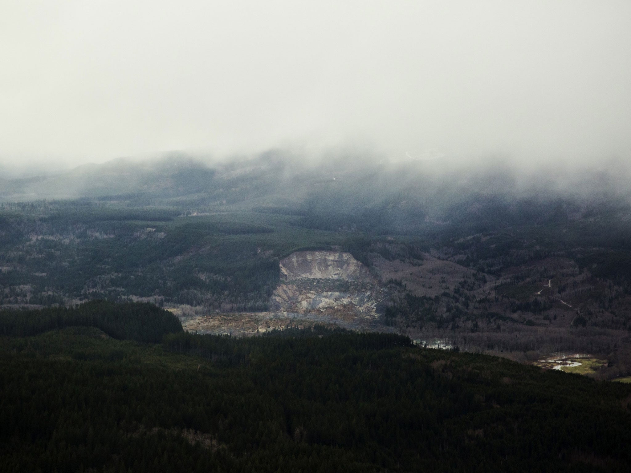 A wide aerial view shows the huge volume of earth missing from the side of a hill facing the Stillaguamish River (AP/Marcus Yam, The Seattle Times)