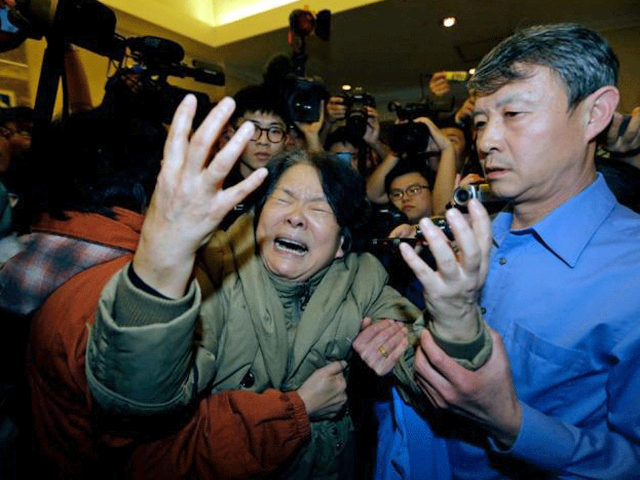 A family member of a passenger aboard Malaysia Airlines MH370 cries as she is surrounded by journalists after watching a television broadcast of a news conference, at the Lido hotel in Beijing