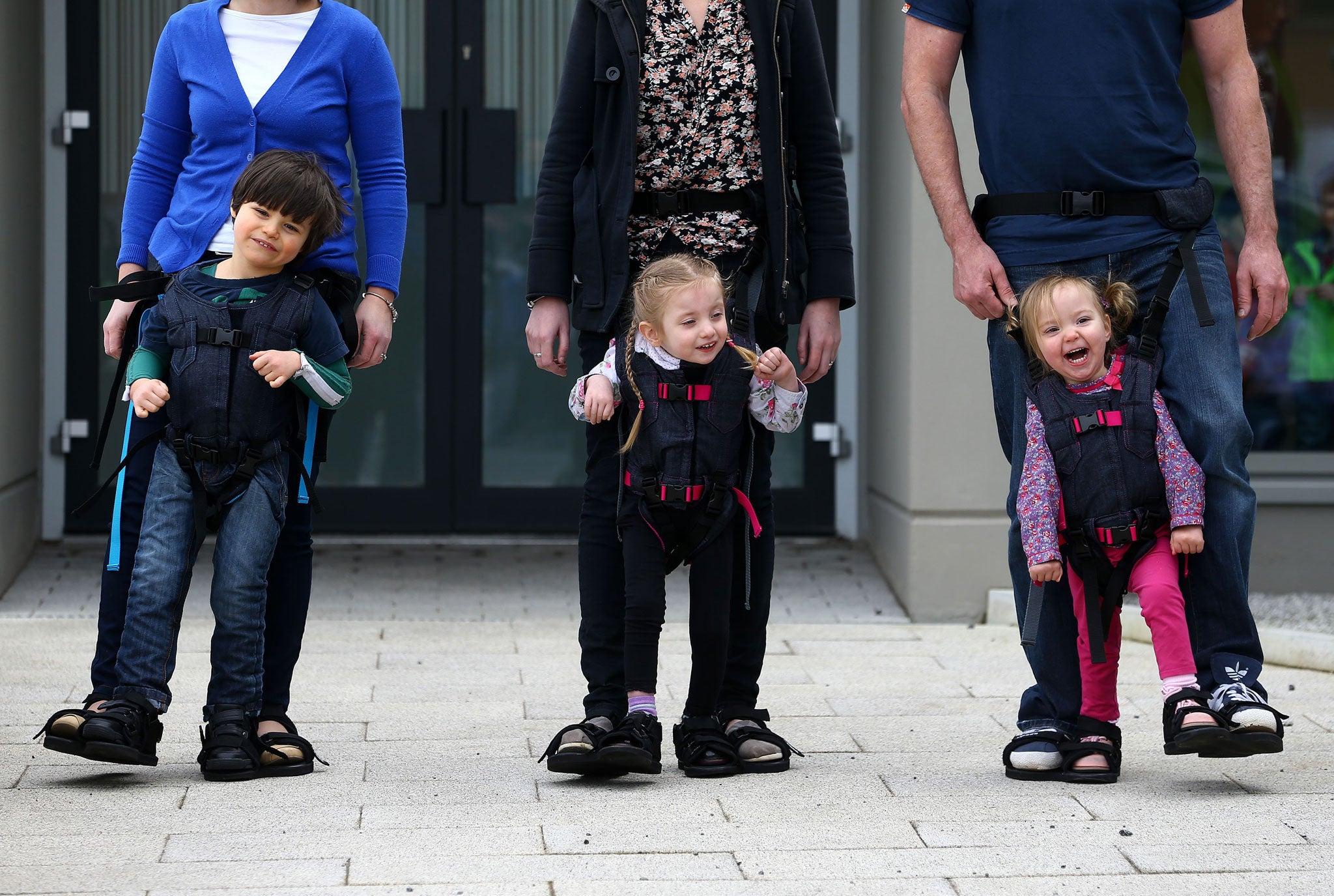 Daniel Smyth, 5, Bethany Watson, 3, and Charlotte Taylor, 3, using a Firefly Upsee, a new standing and walking harness for children with motor impairment, which attaches to a parent, allowing them and their child to take steps together