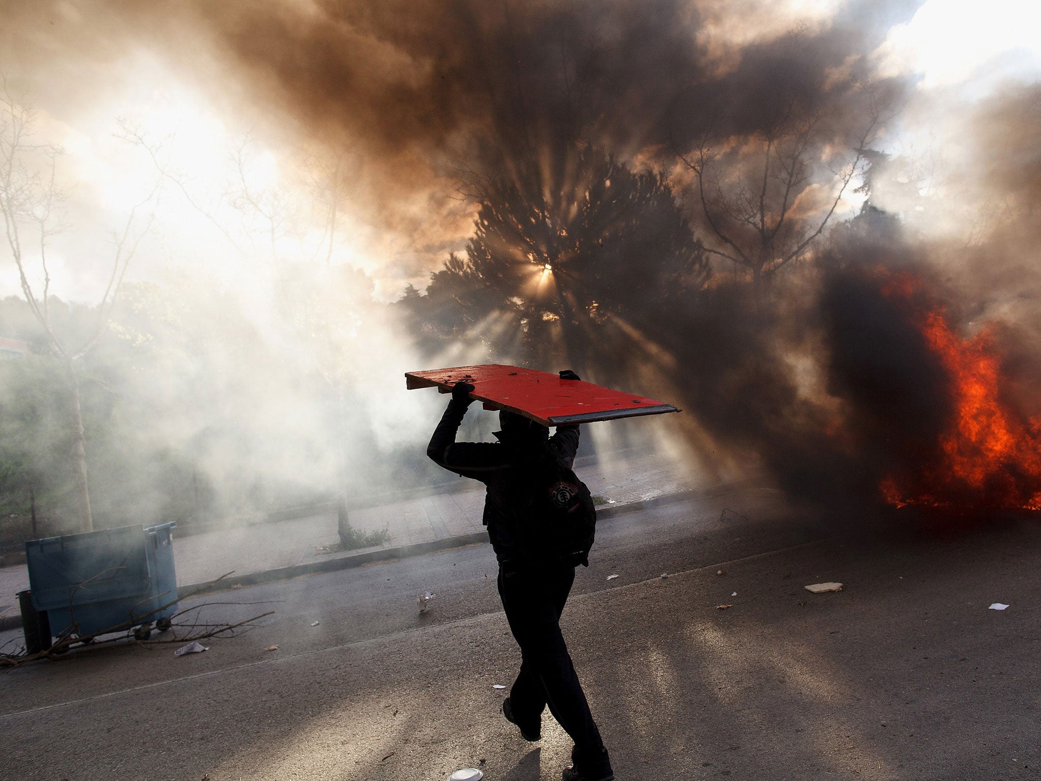 A protester carries a wooden table as he walks next to a burning barricade during a protest against the government's education reforms and cutbacks in university grants and staffing in Campus Ciudad Universitaria in Madrid