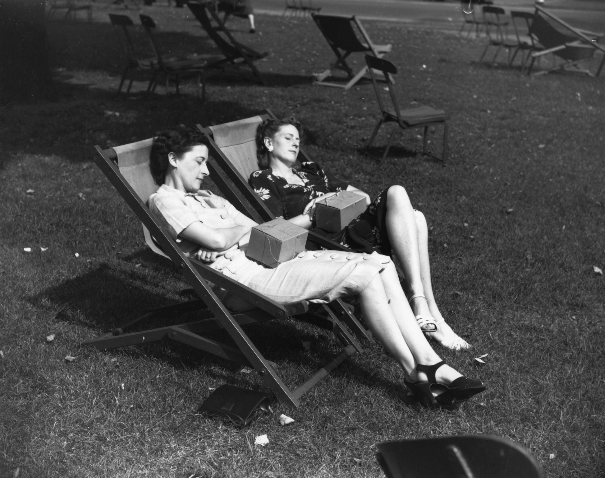 A couple of lady office workers with gas-masks on their laps, sleeping peacefully in Hyde Park during their lunch hour in September 1939.